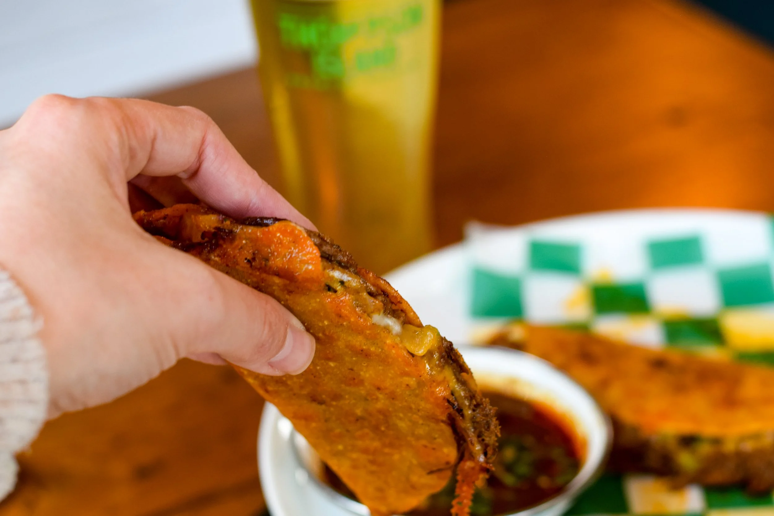 Close-up of a hand holding a birria taco with a dipping sauce in the background.