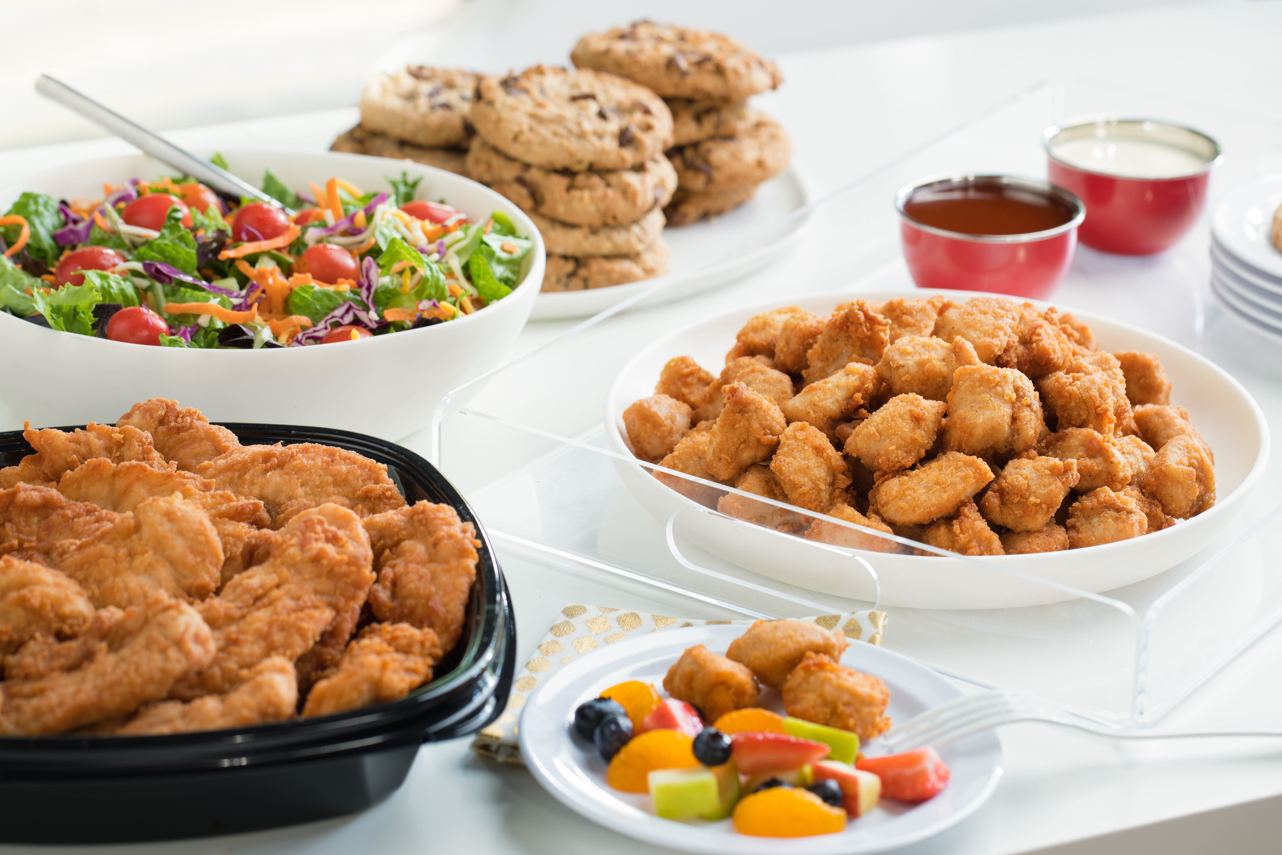 Chick-fil-A strips, nuggets, salad and cookies in serving bowls.