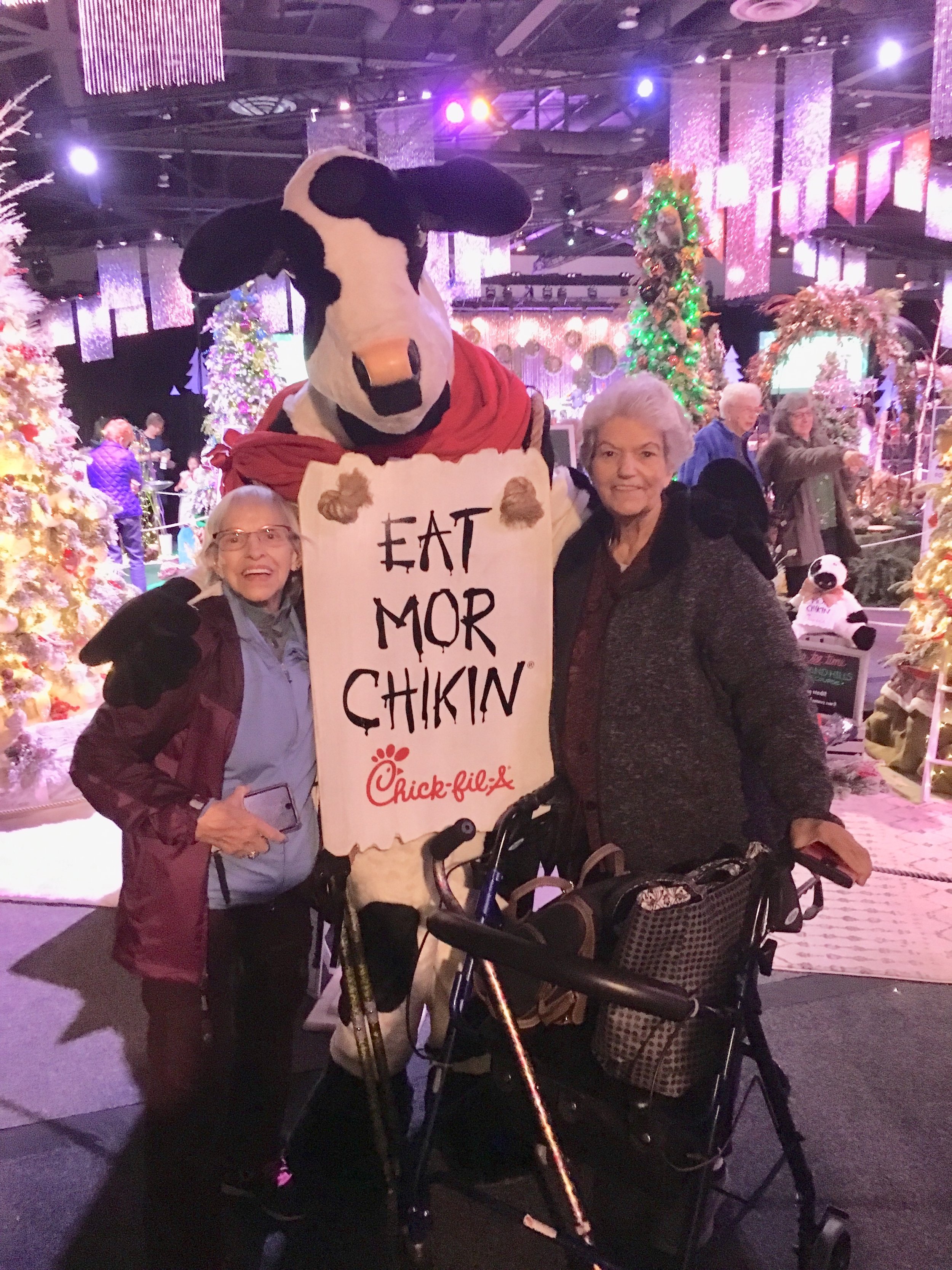 Two women with Chick-fil-A cow in front of Christmas trees