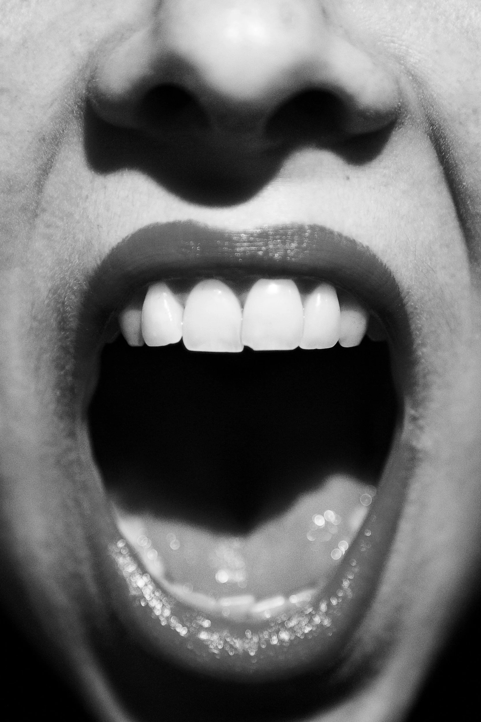 Close-up of a person's open mouth, showing teeth and tongue, in black and white.