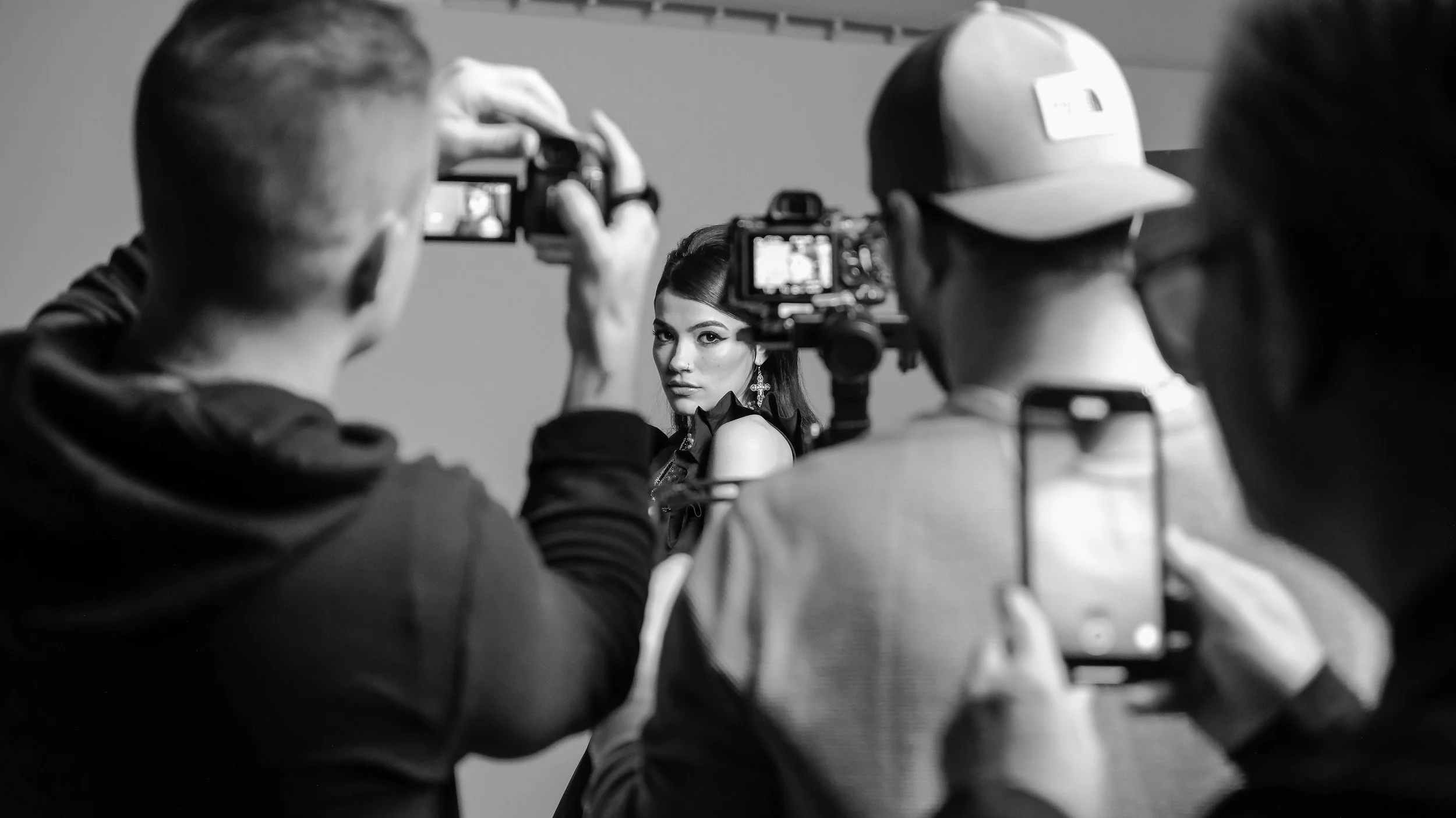 A female model getting photographed by a team of photographers in a studio, black and white.