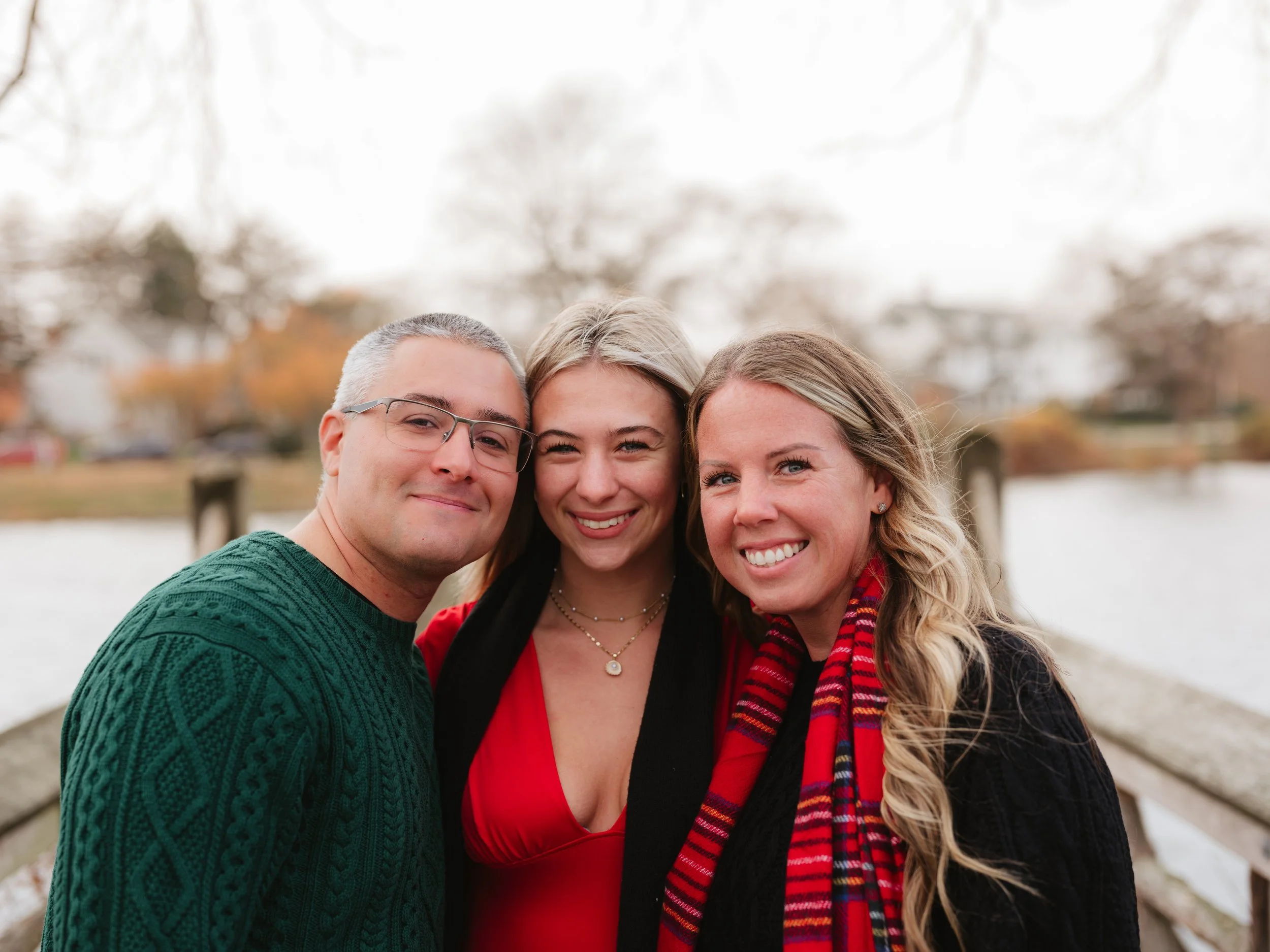 Three smiling people standing on a bridge near a river with trees in fall colors in the background.