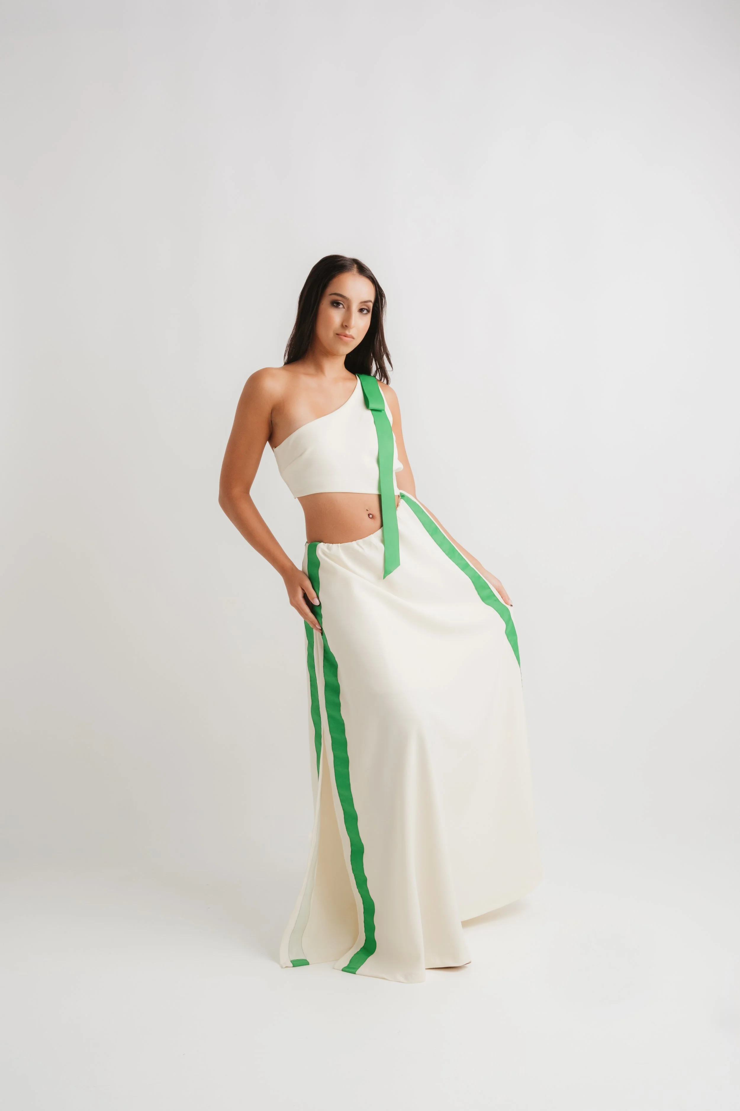 A young woman with long dark hair wearing a cream-colored two-piece outfit with green stripes, standing against a white background.