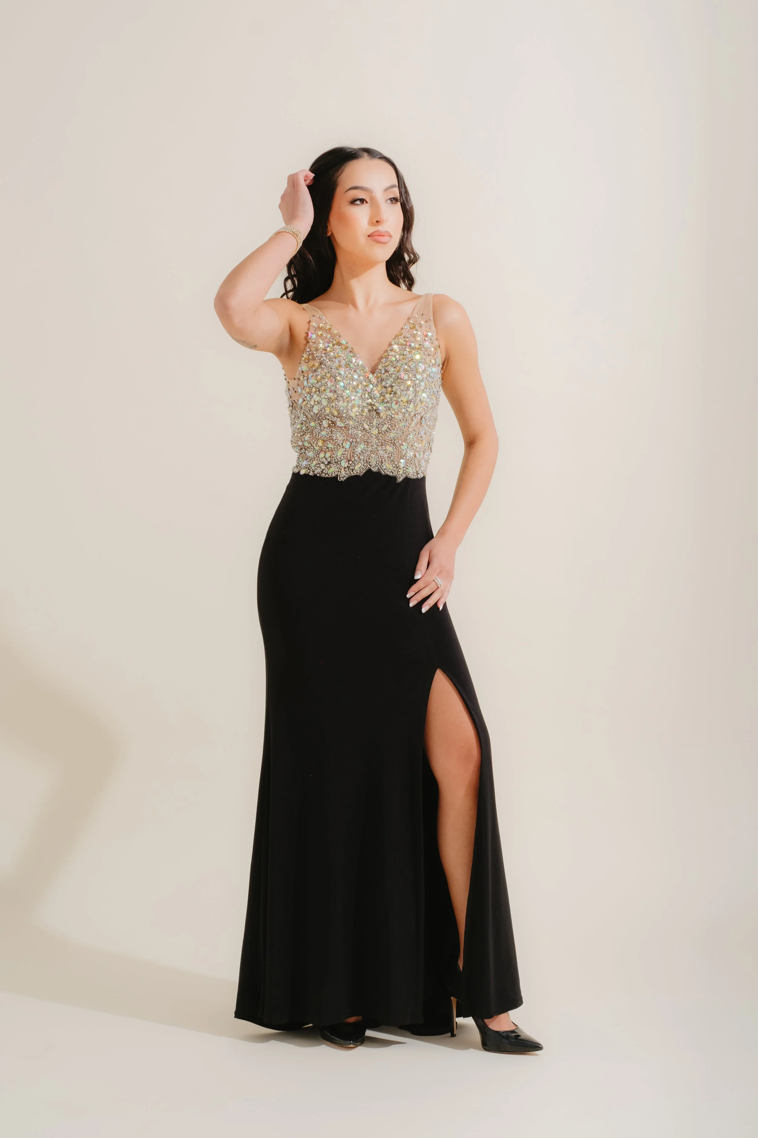 Woman in an evening gown with a beaded top and high slit, posing against a plain background.