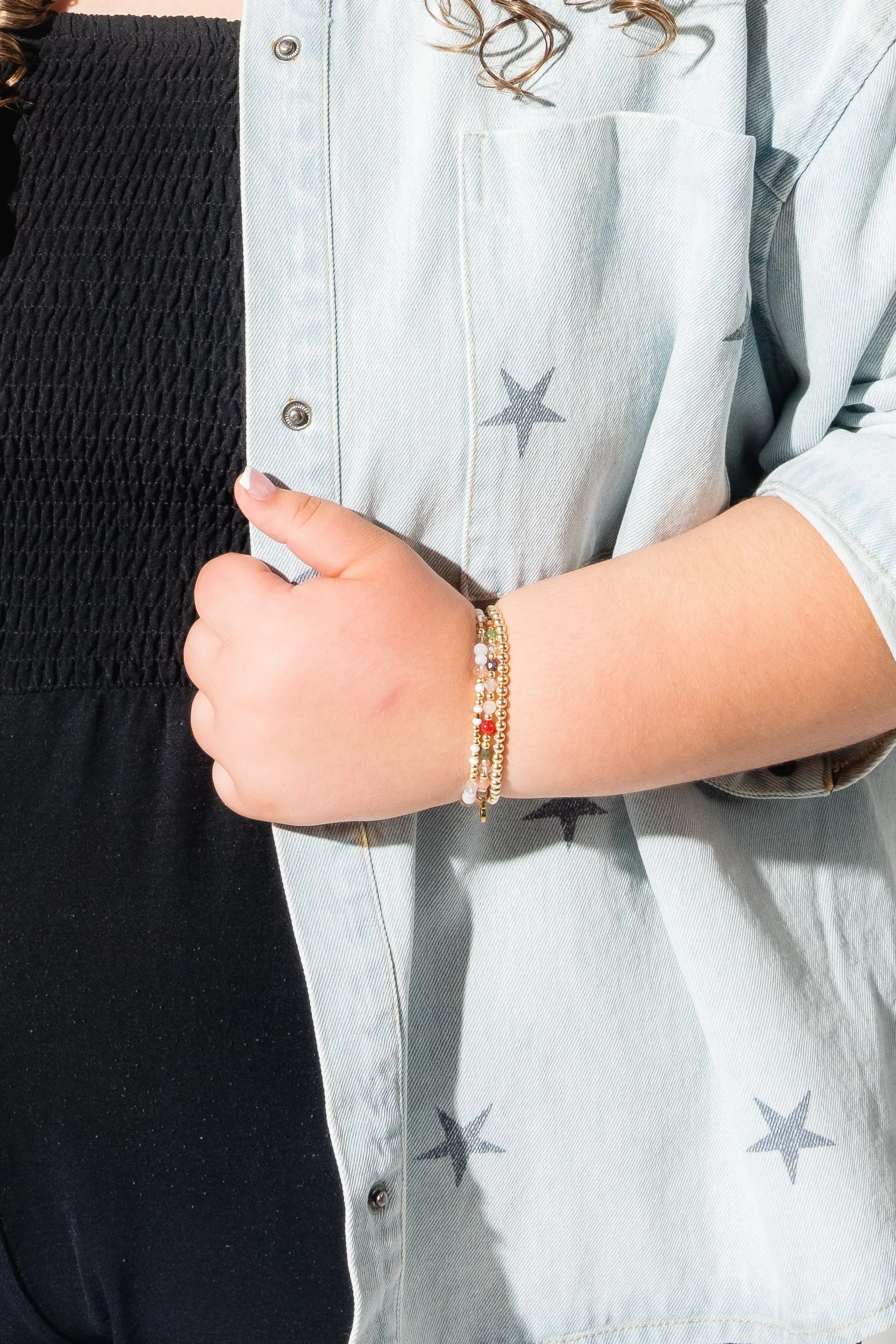 Close-up of two people showing their arms and torsos. One person is wearing a black textured garment and the other is wearing a light denim shirt with star patterns and beaded bracelets on their wrist.