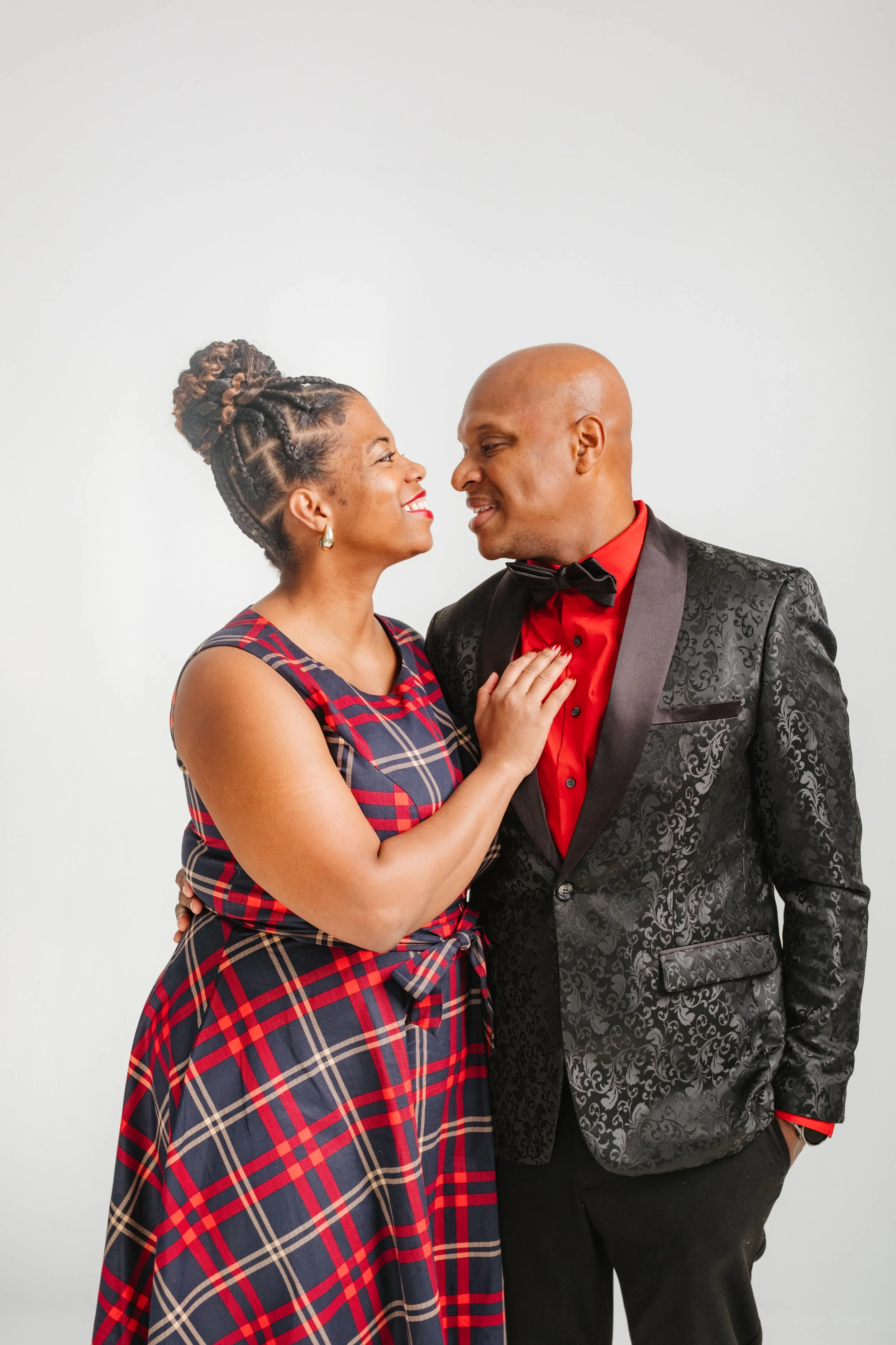 A happy couple in formal attire looking at each other, standing close with the woman touching the man's chest.