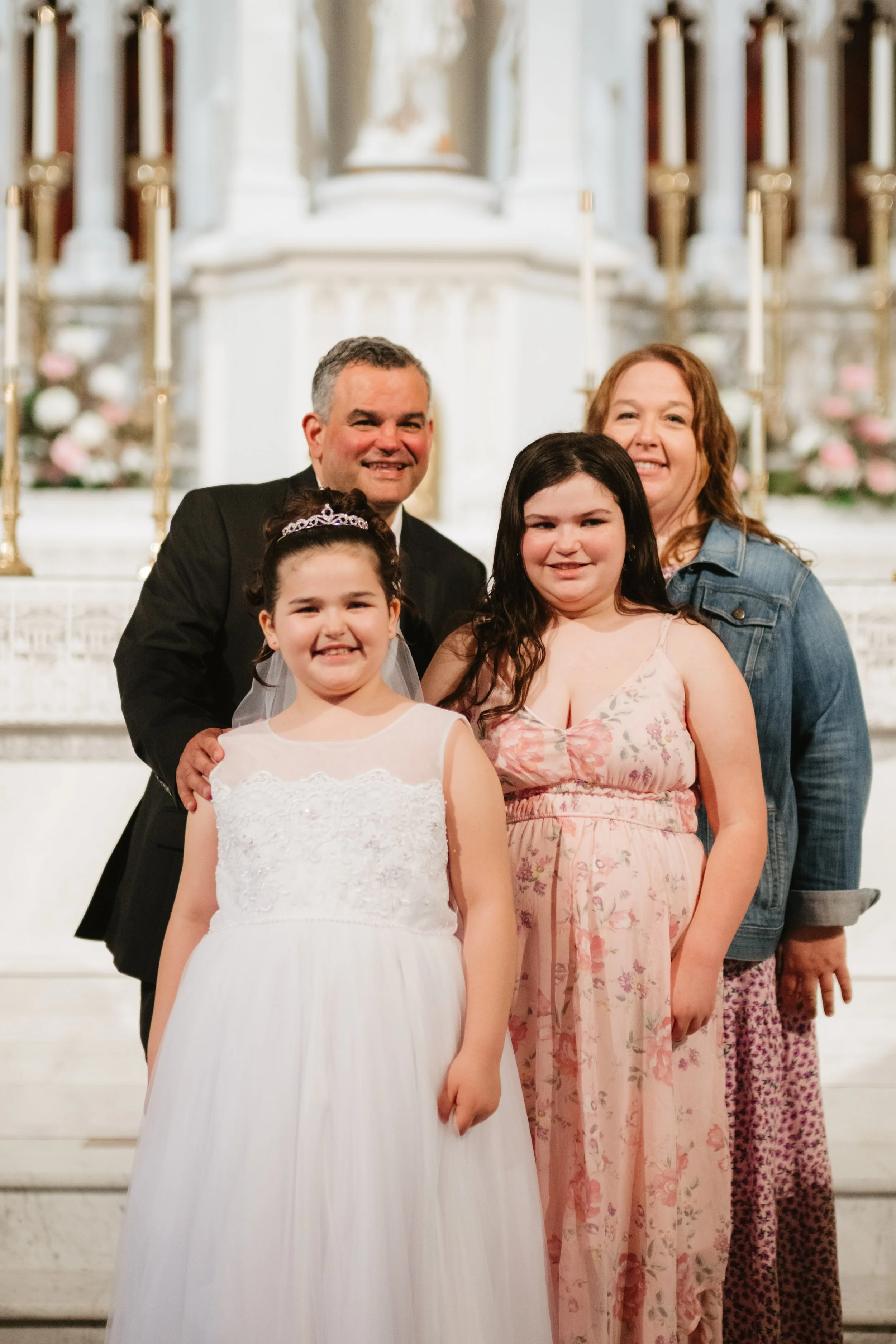A family of four posing on church stairs; a man and woman with two young girls, all smiling.