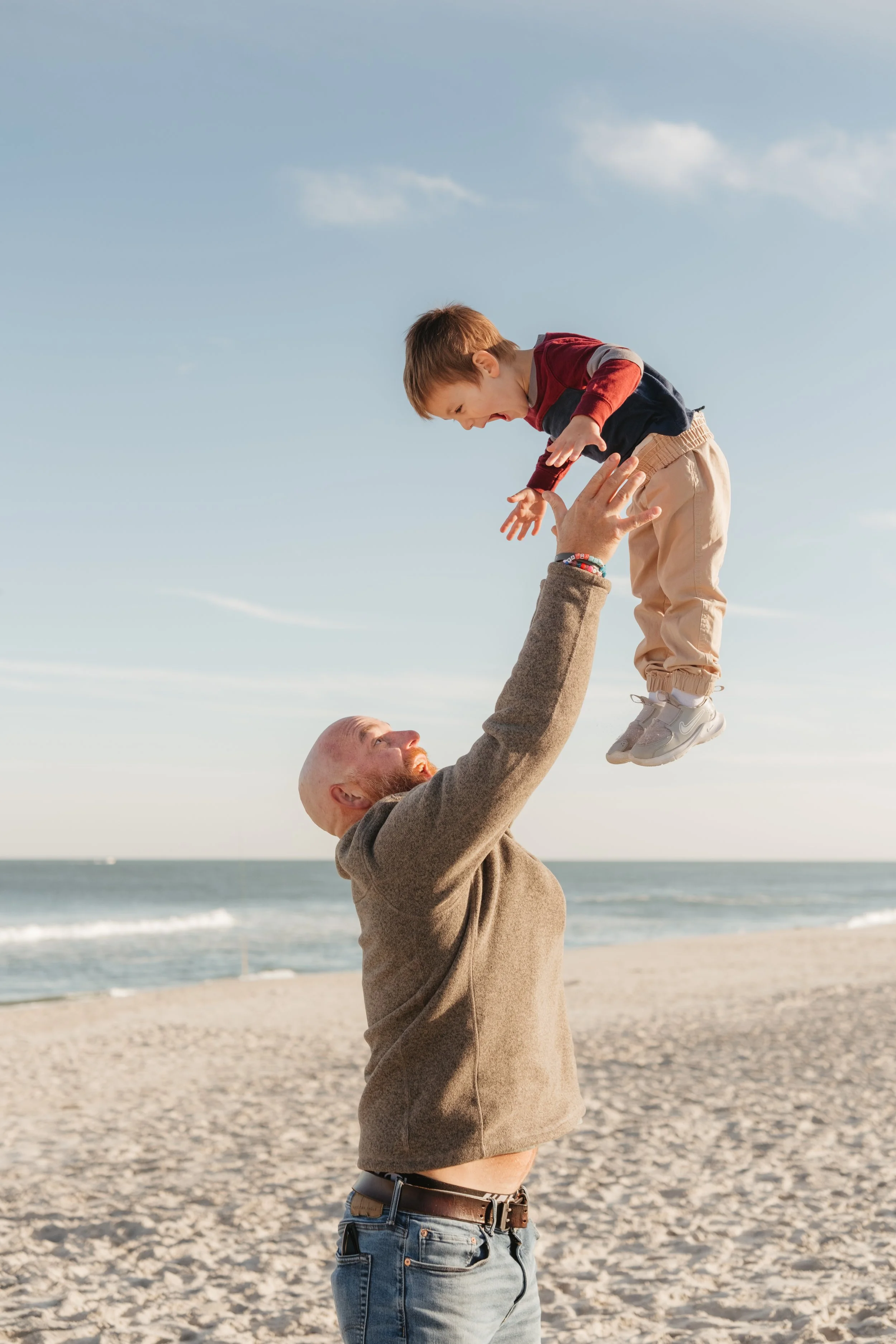 A man lifting a young boy into the air on a beach during daytime.