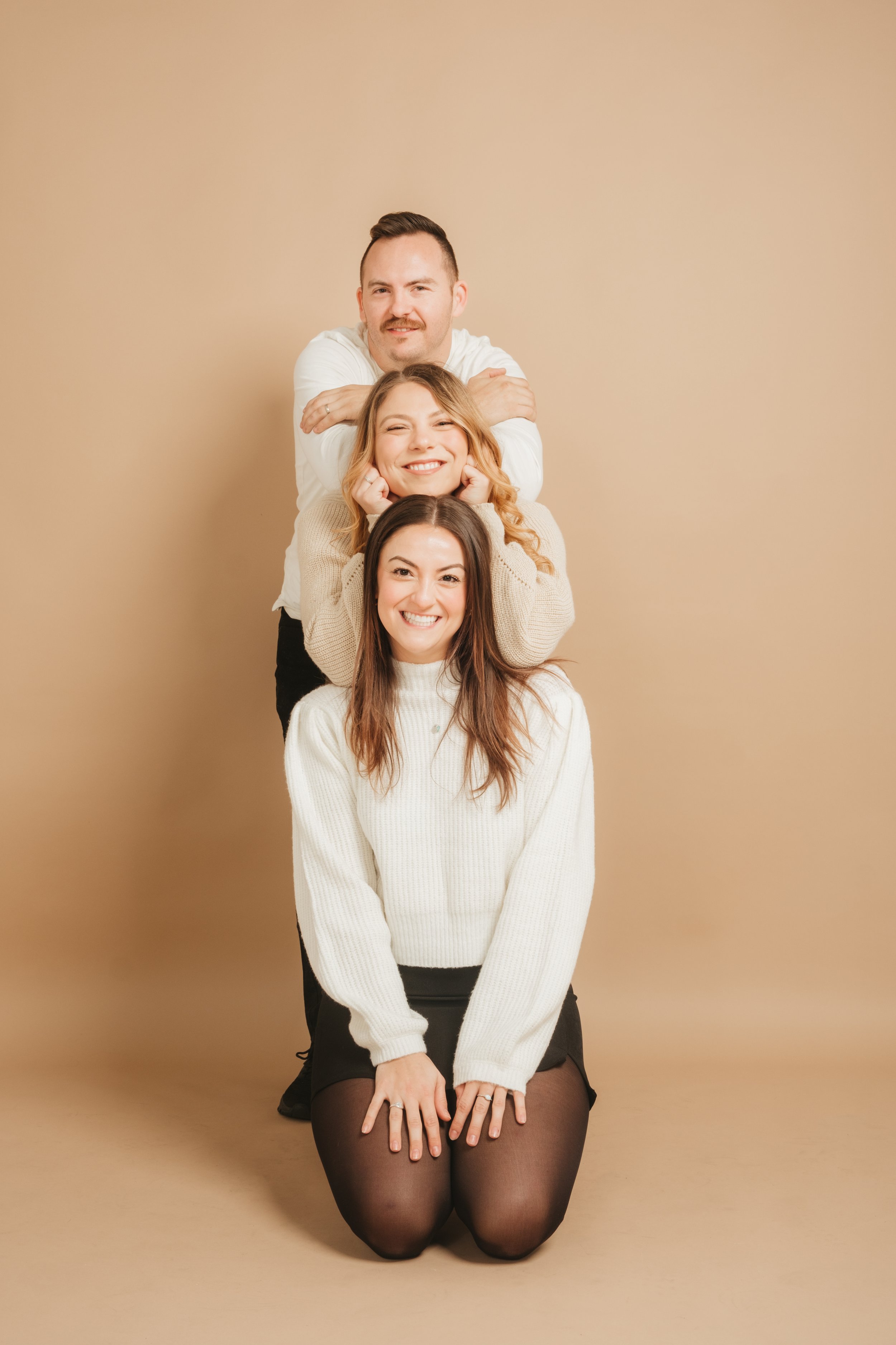 Four people stacked in a line, smiling, with the woman in front kneeling on the ground, and the others behind her in a playful pose.