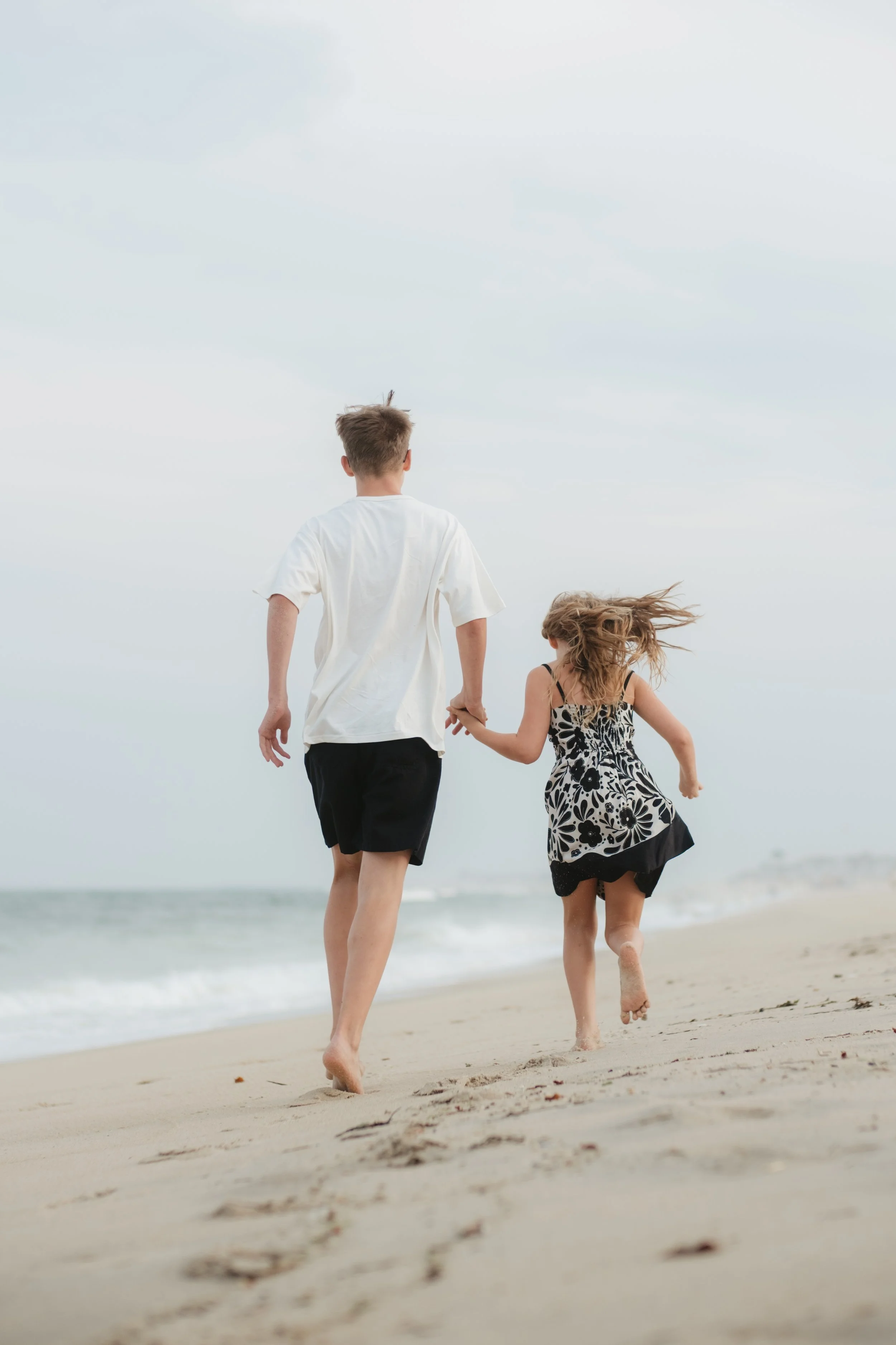 A boy and a girl holding hands while running on a beach.
