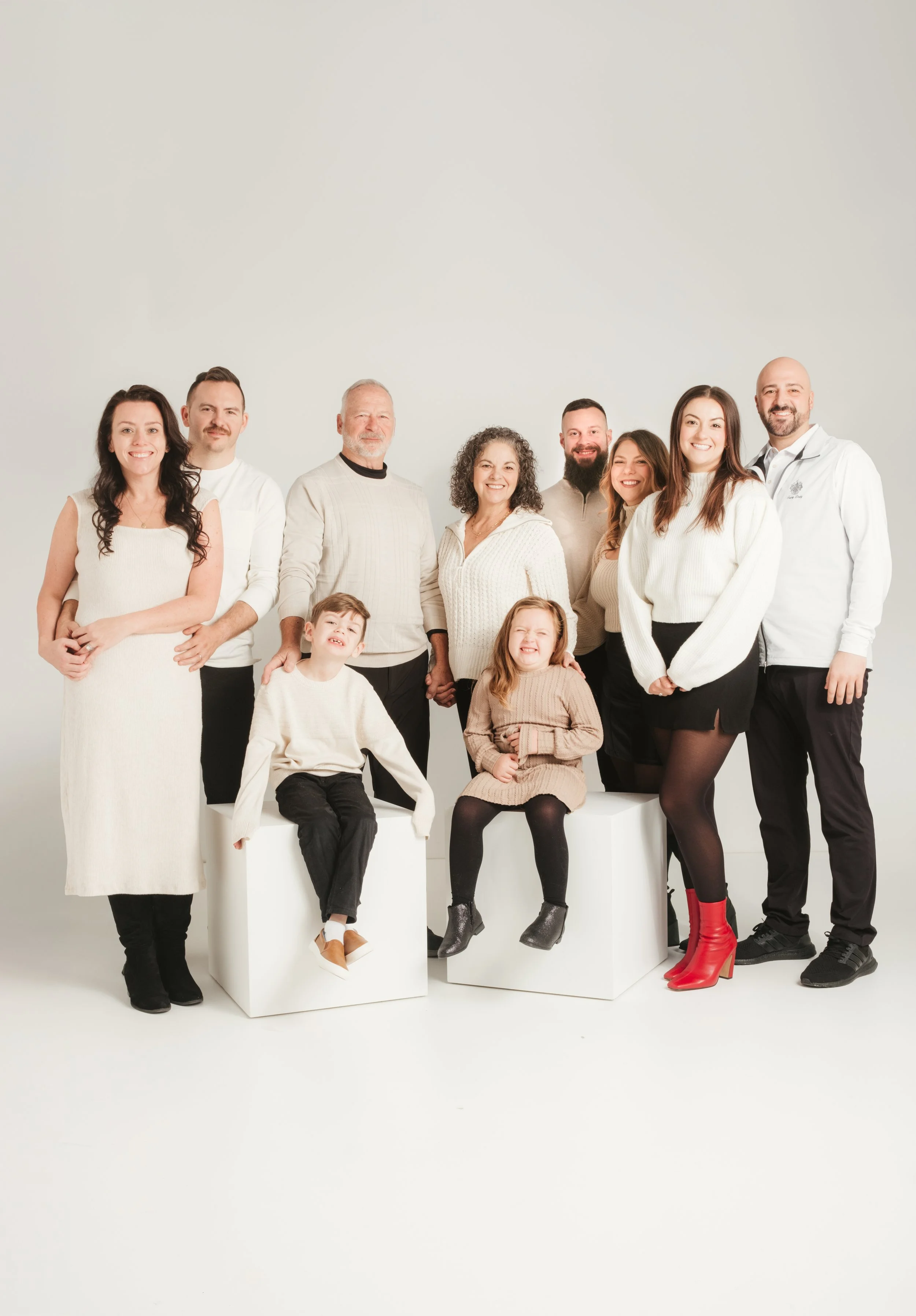 Family group photo with adults and children wearing neutral-colored clothing against a plain background.