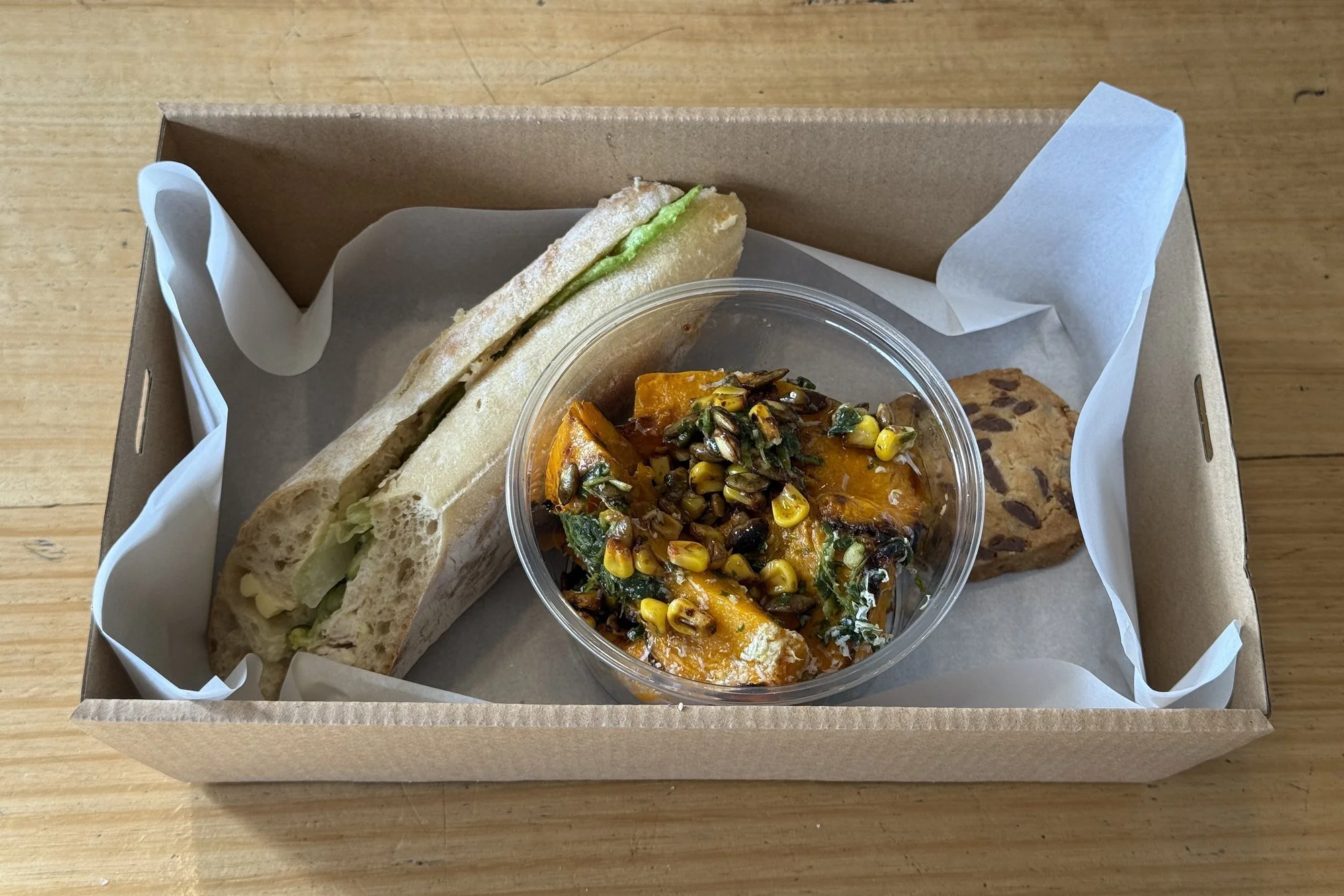 An individually packed Marché lunch box with a half baguette, seasonal salad and a sweet treat
