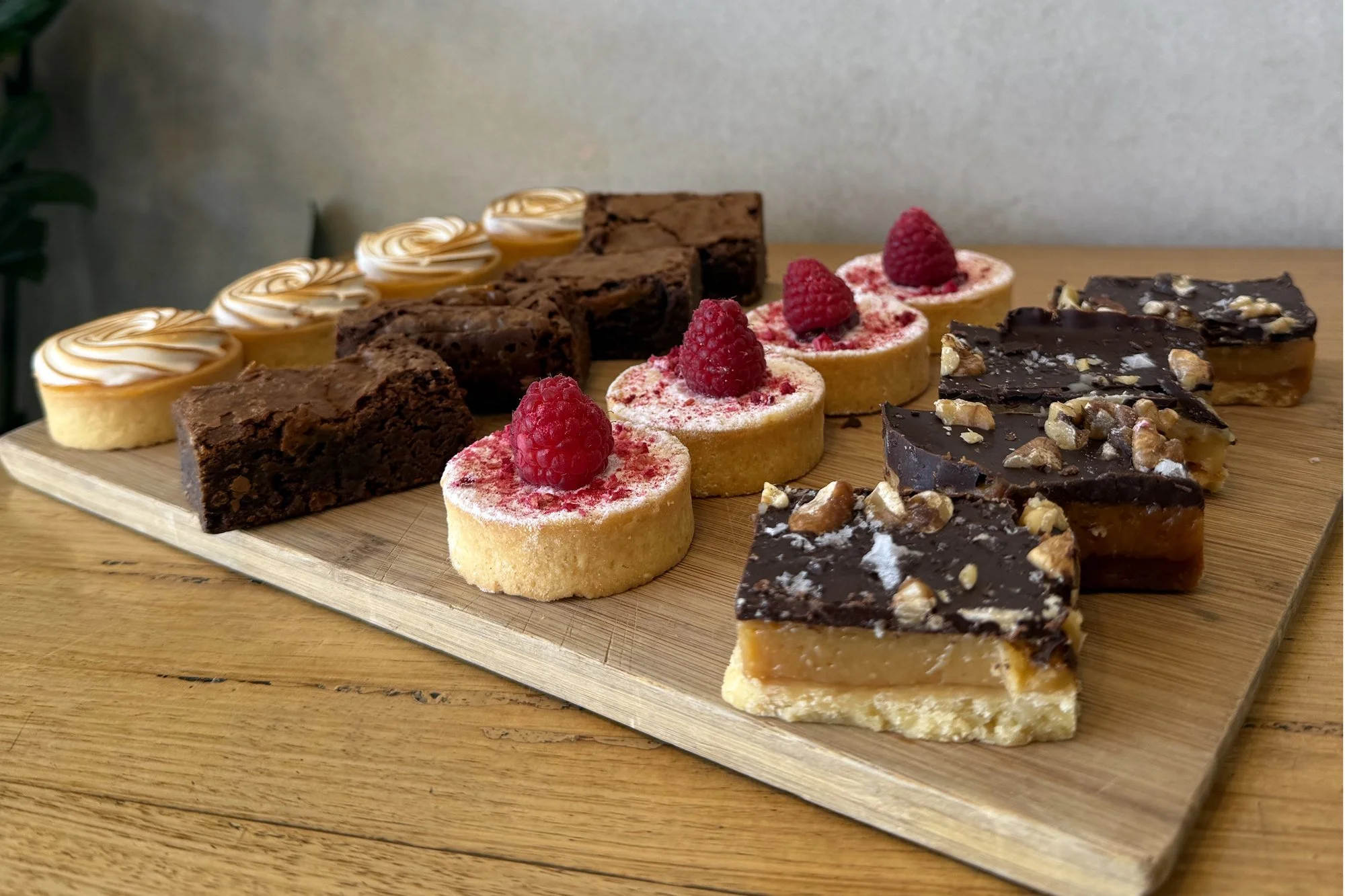 Marché sweet box — lemon meringue tarts, brownies, raspberry cheesecakes and caramel slice on a wooden board