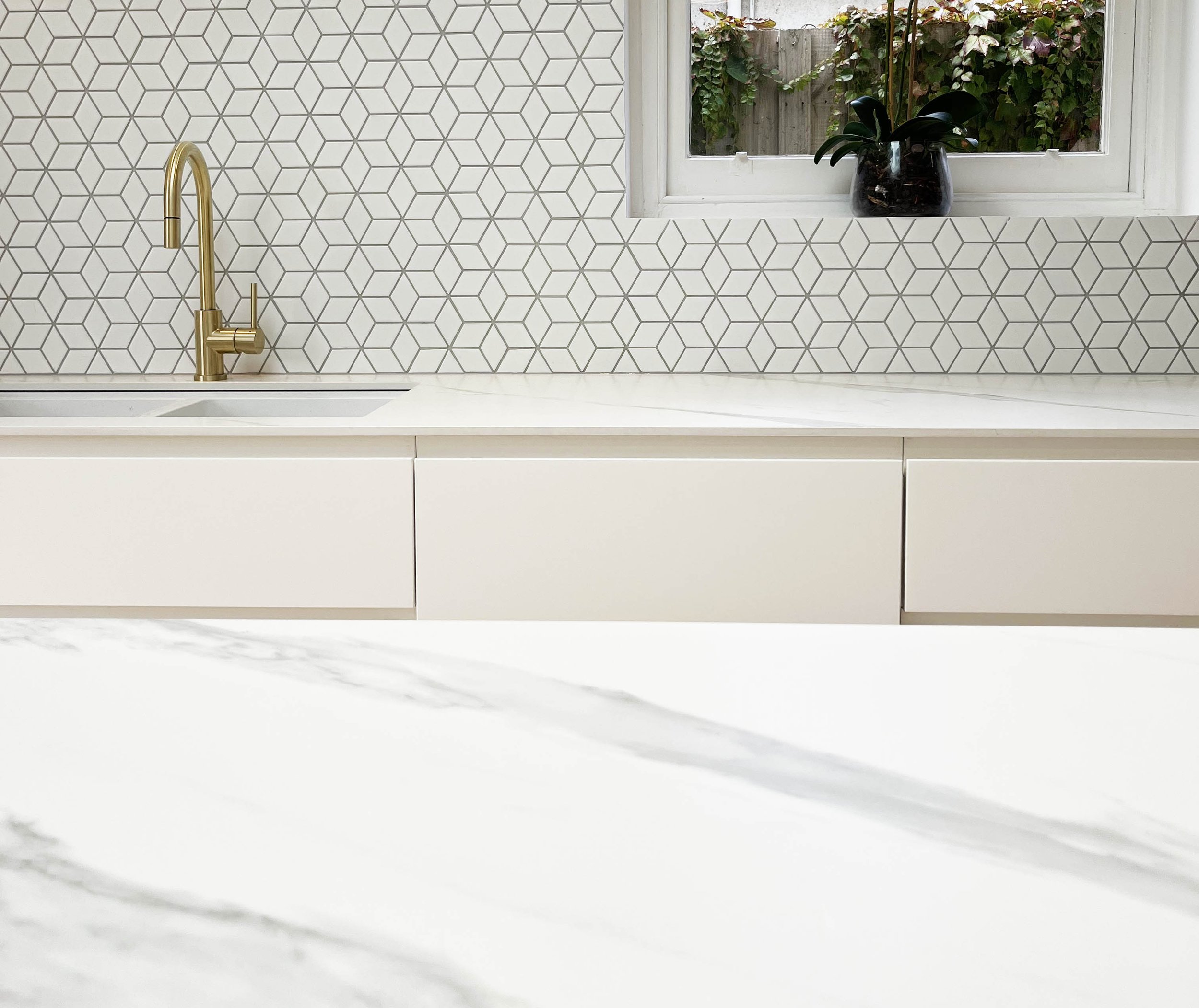brass kitchen taps, triangular splashback tiles and stone bench surface