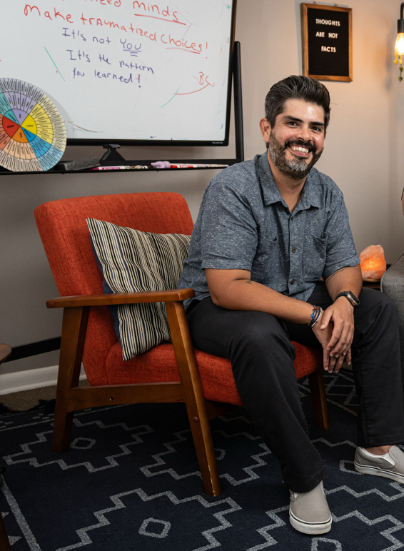 Derrick Miller, a therapist at Labyrinth PLLC, sitting in a chair in his office with a whiteboard visible in the background.
