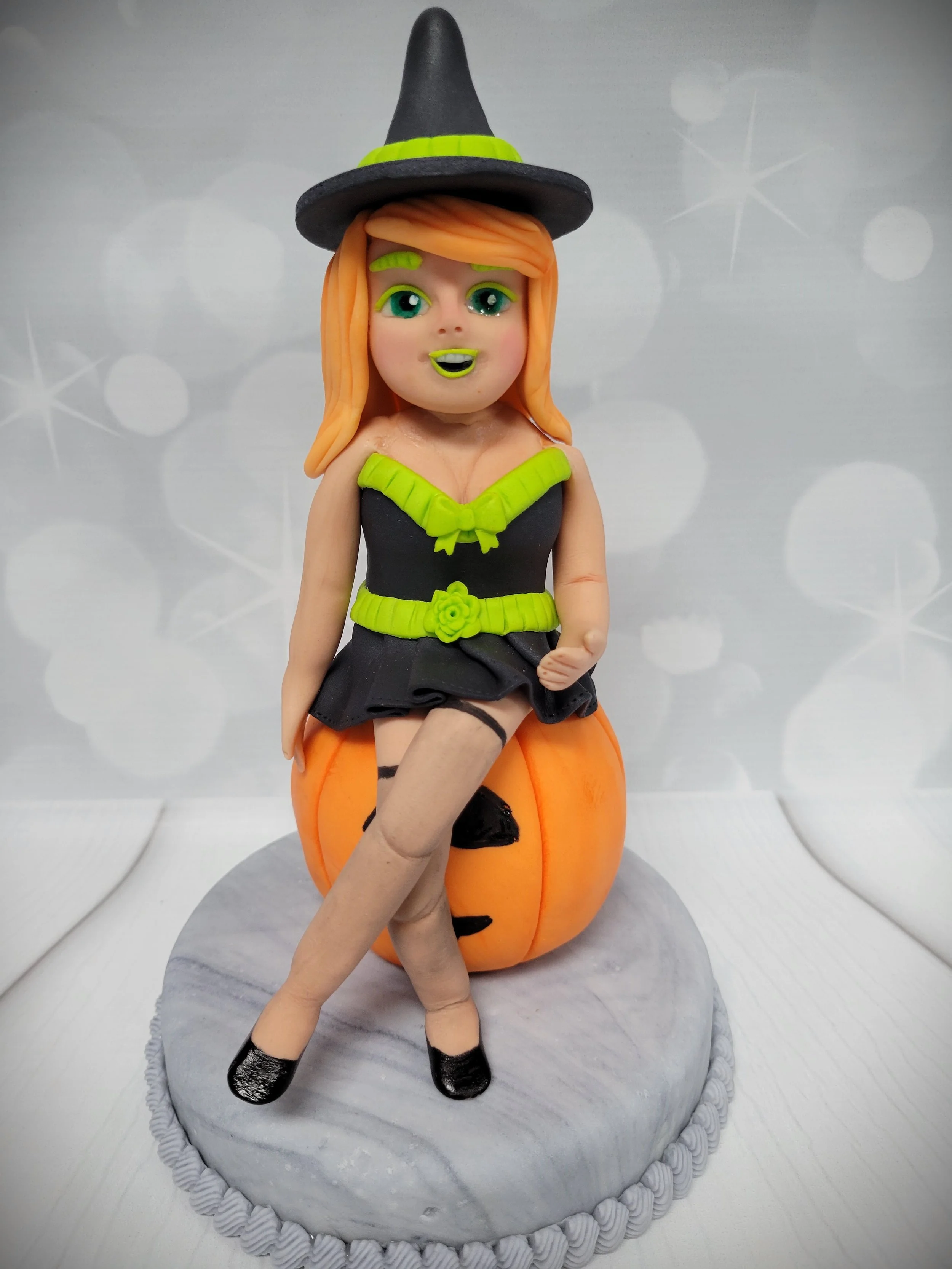 Cake topper of a witch sitting on a pumpkin
