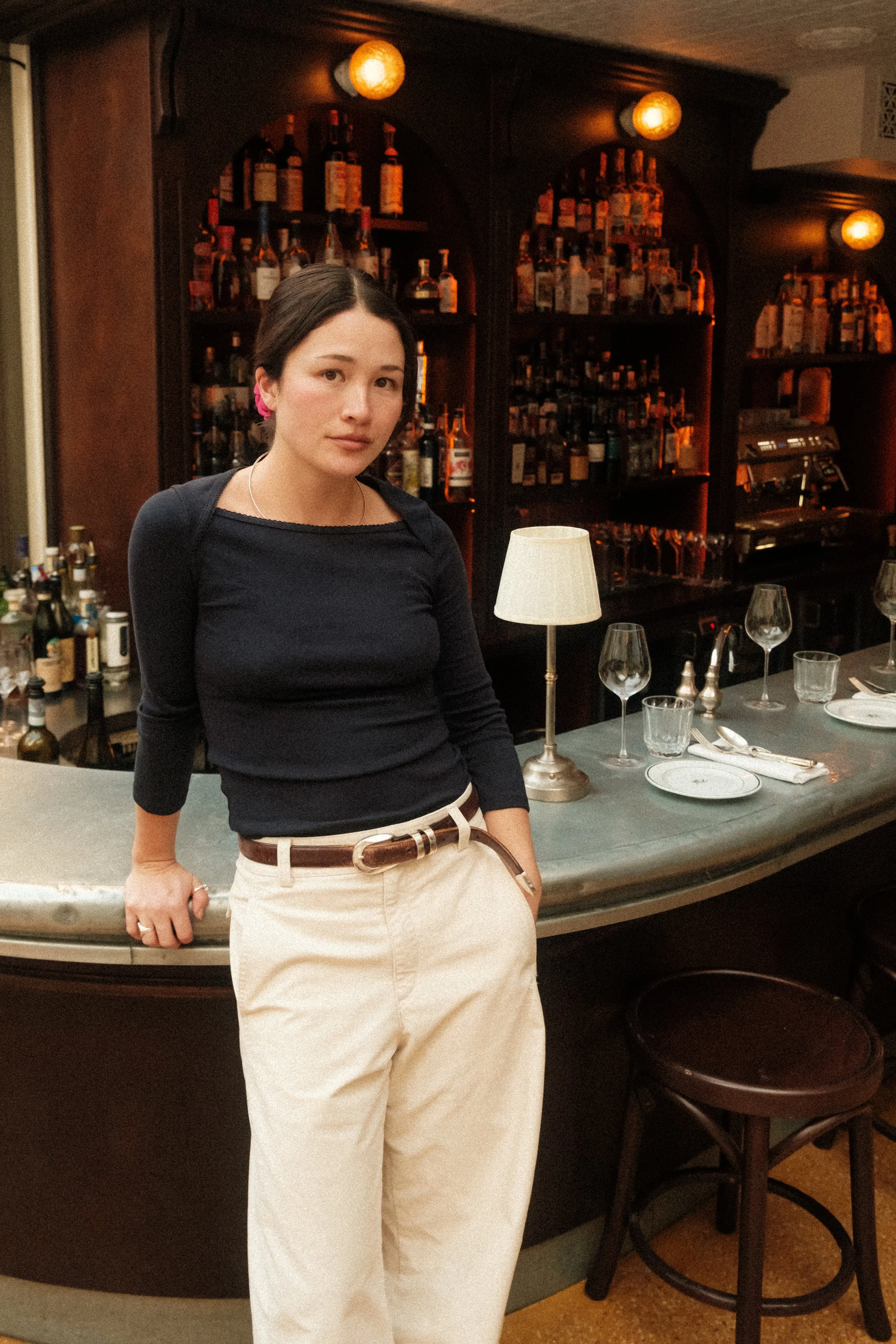 A woman standing beside a bar counter in a dimly lit bar with a timeless decor, interior designer