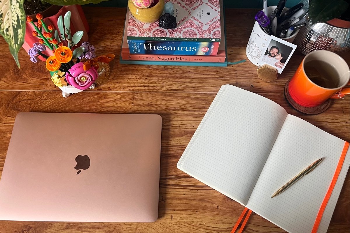 Photo od a desk with a laptop, notebook and pen, cup of tea, books and other accessories