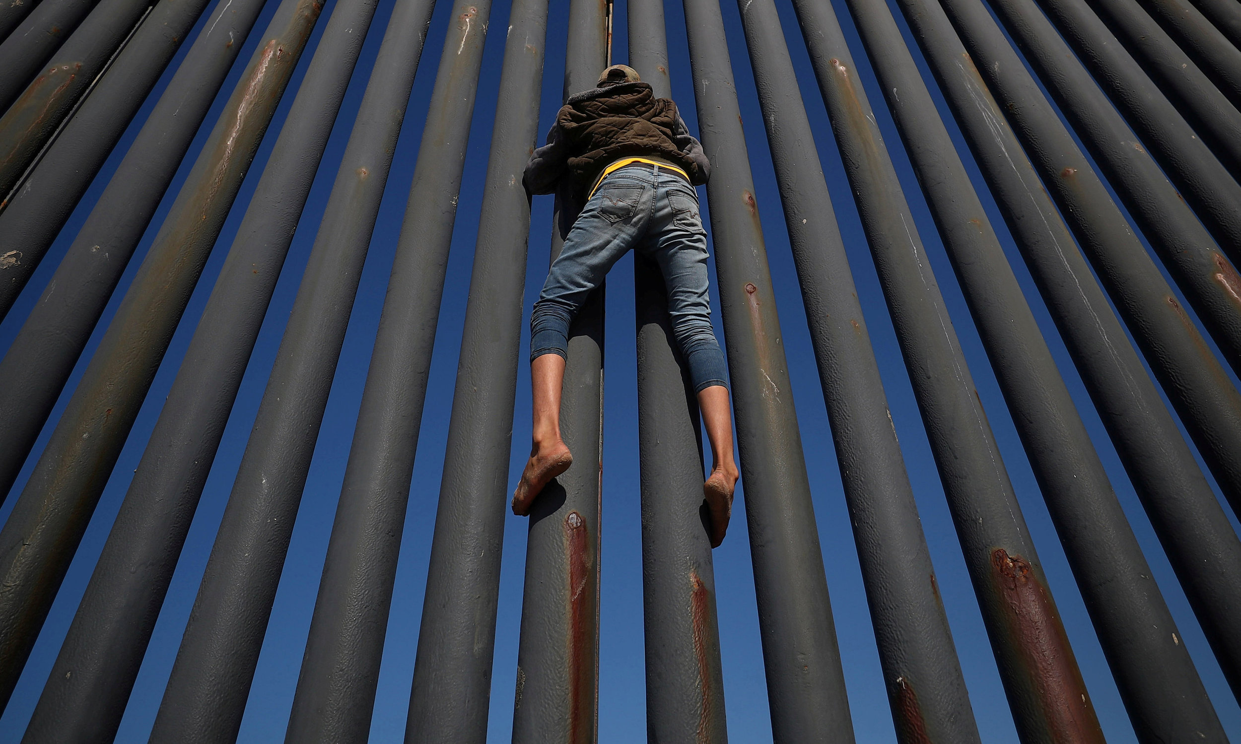  A migrant, part of a caravan of thousands from Central America trying to reach the United States, climbs the border fence between Mexico and the United States, in Tijuana, Mexico.
Photo by Hannah McKay, 18 November 2018
 