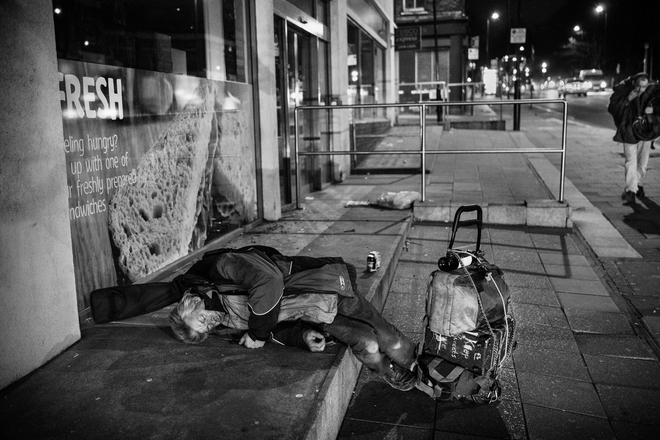 A homeless man lays on Pentonville Road in London, apparently passed out from drinking the wine tied to the top of his belongings on his trolley. His guitar is still strapped to his back. 
Photo by Edmond Terakopian, 21 March 2018
 
