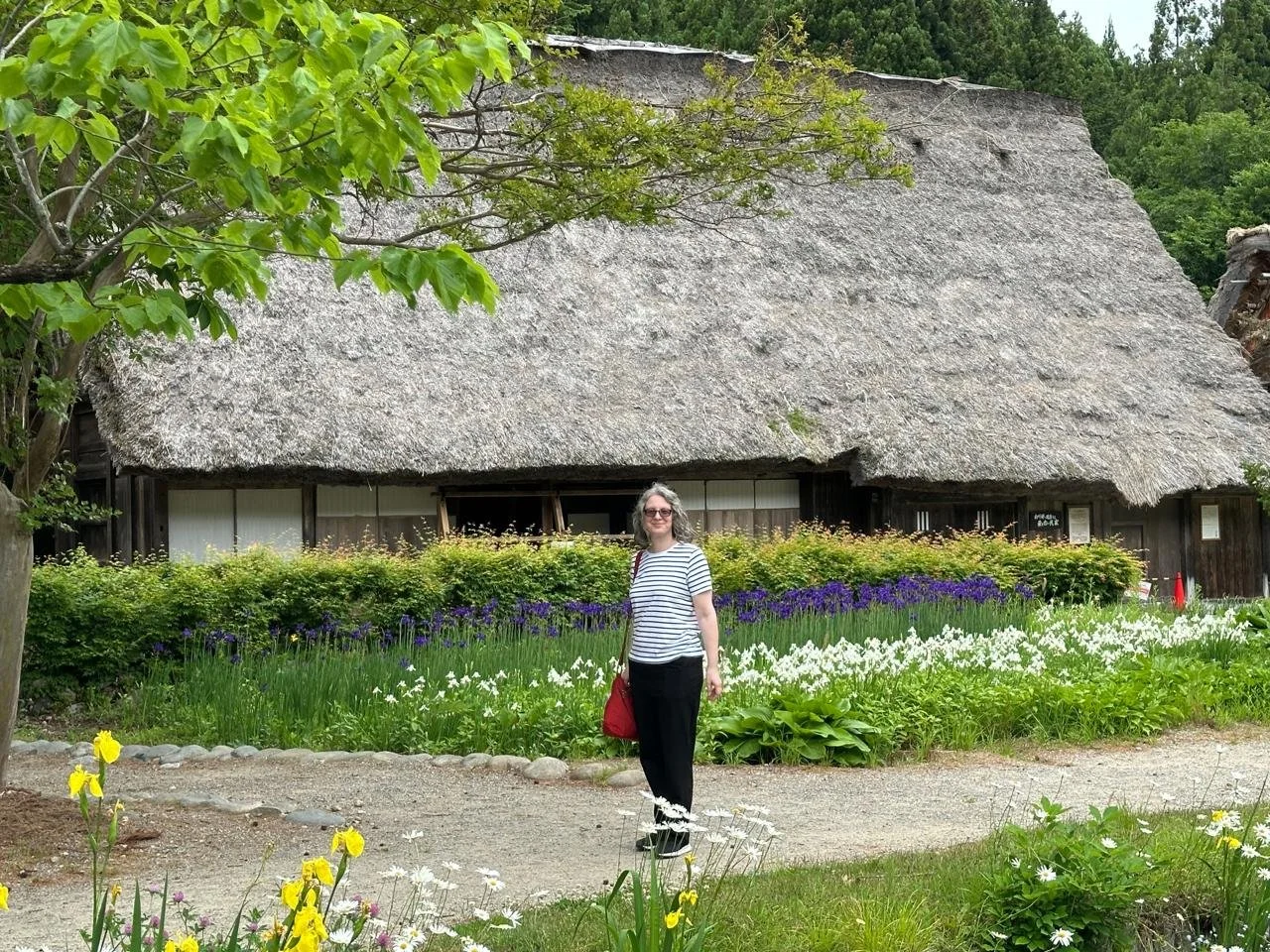 Amélie standing in front of a thatched roof house with beautiful irises