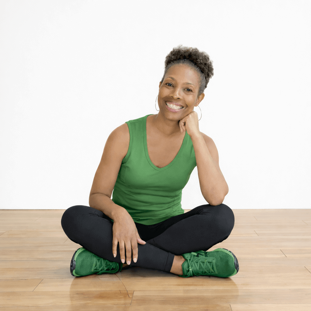smiling woman sitting Indian style wearing green tank top, grey stretch pants, and green sneakers