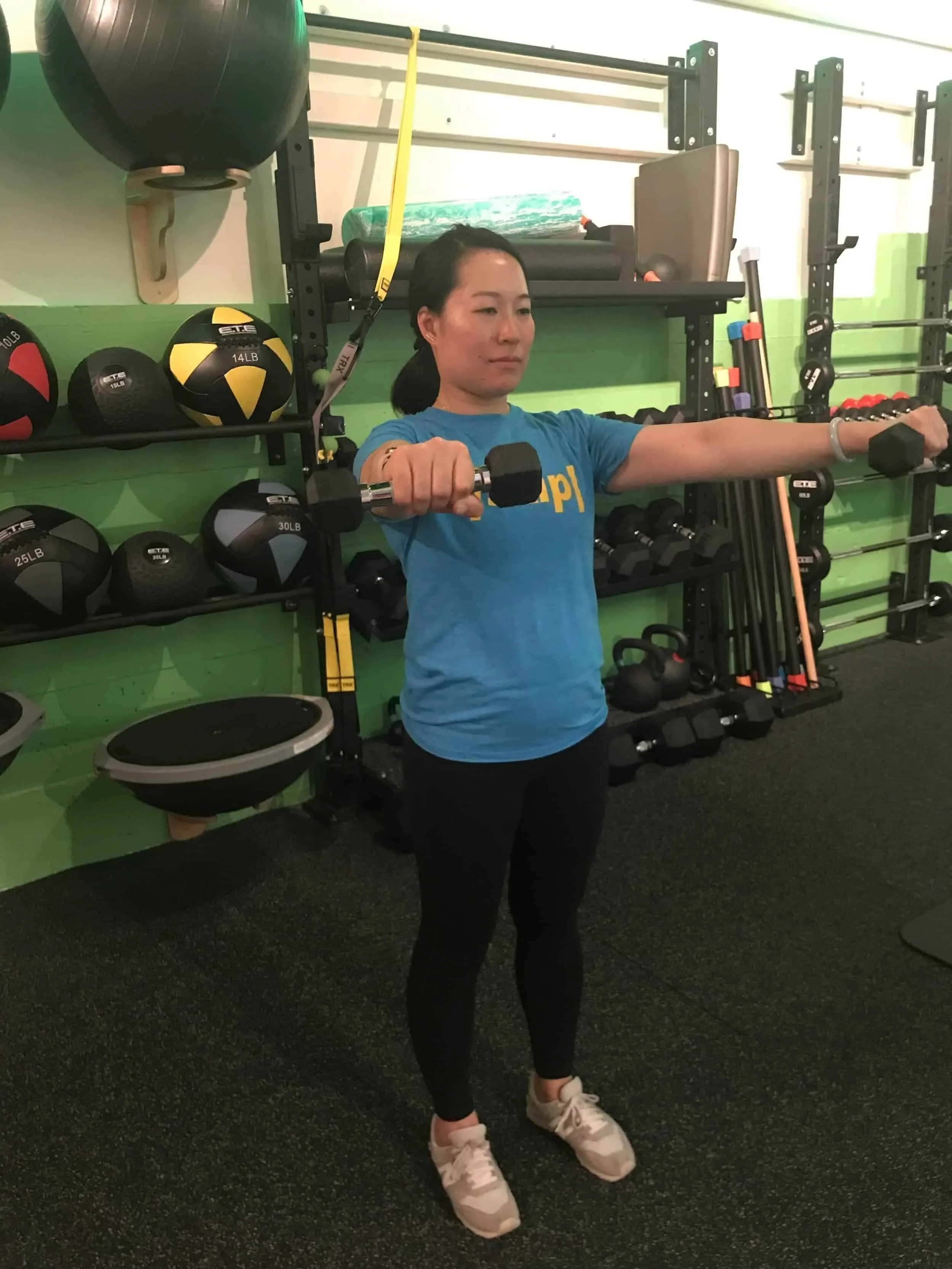 Woman doing dumbbell lateral raises at Eden Fitness Studio women-only gym in San Francisco with green walls and equipment