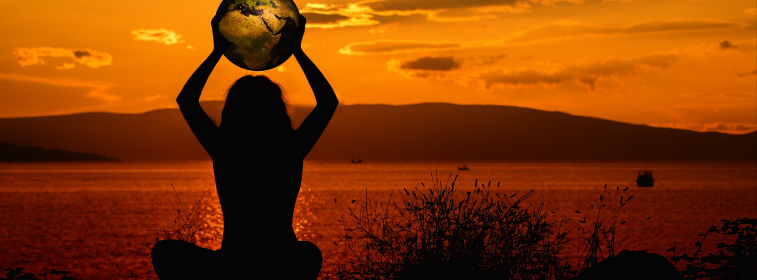 woman sitting holding globe to sky at sunset.png