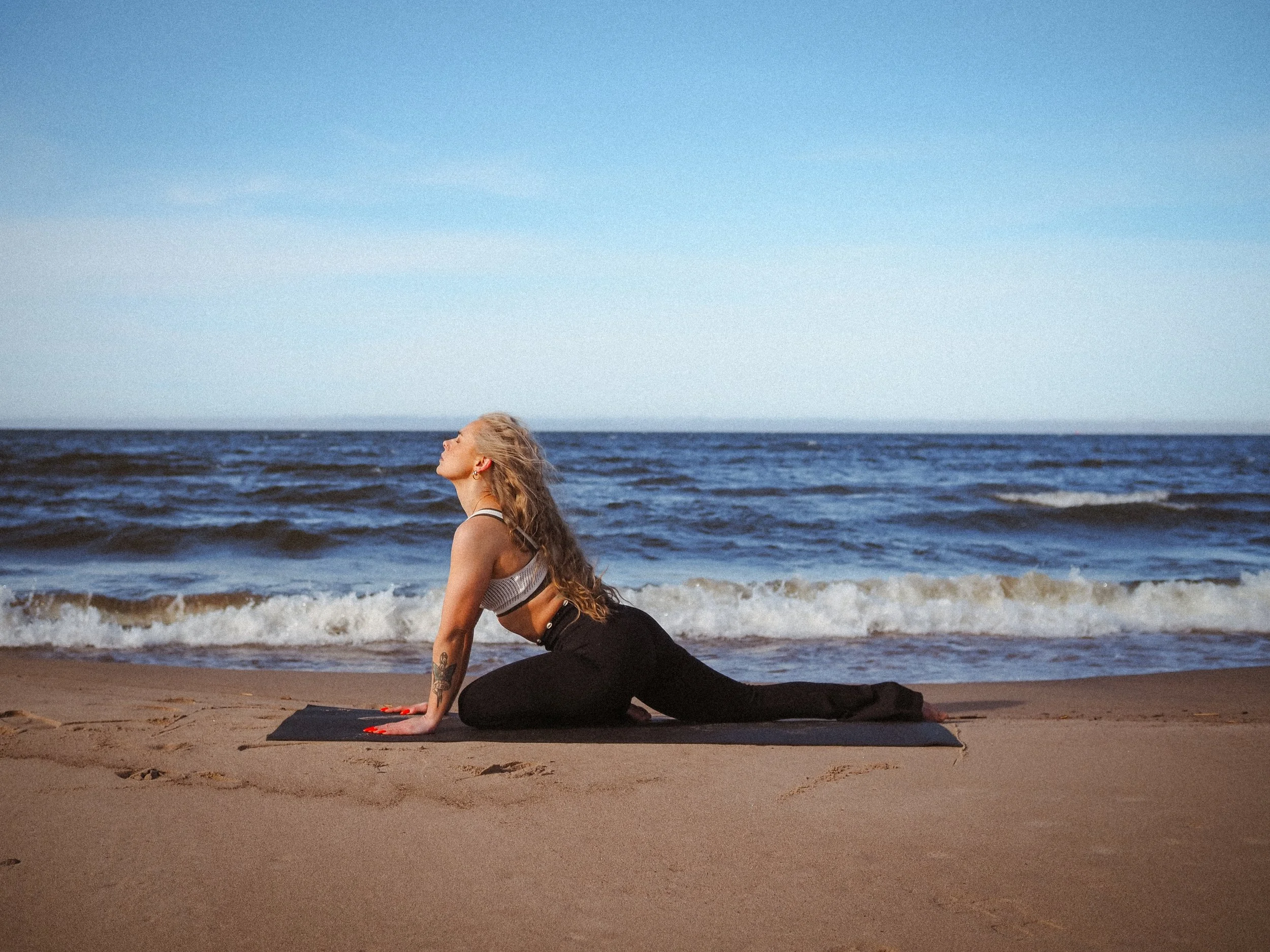 Nainen tekee joogaliikettä rannalla meren äärellä.