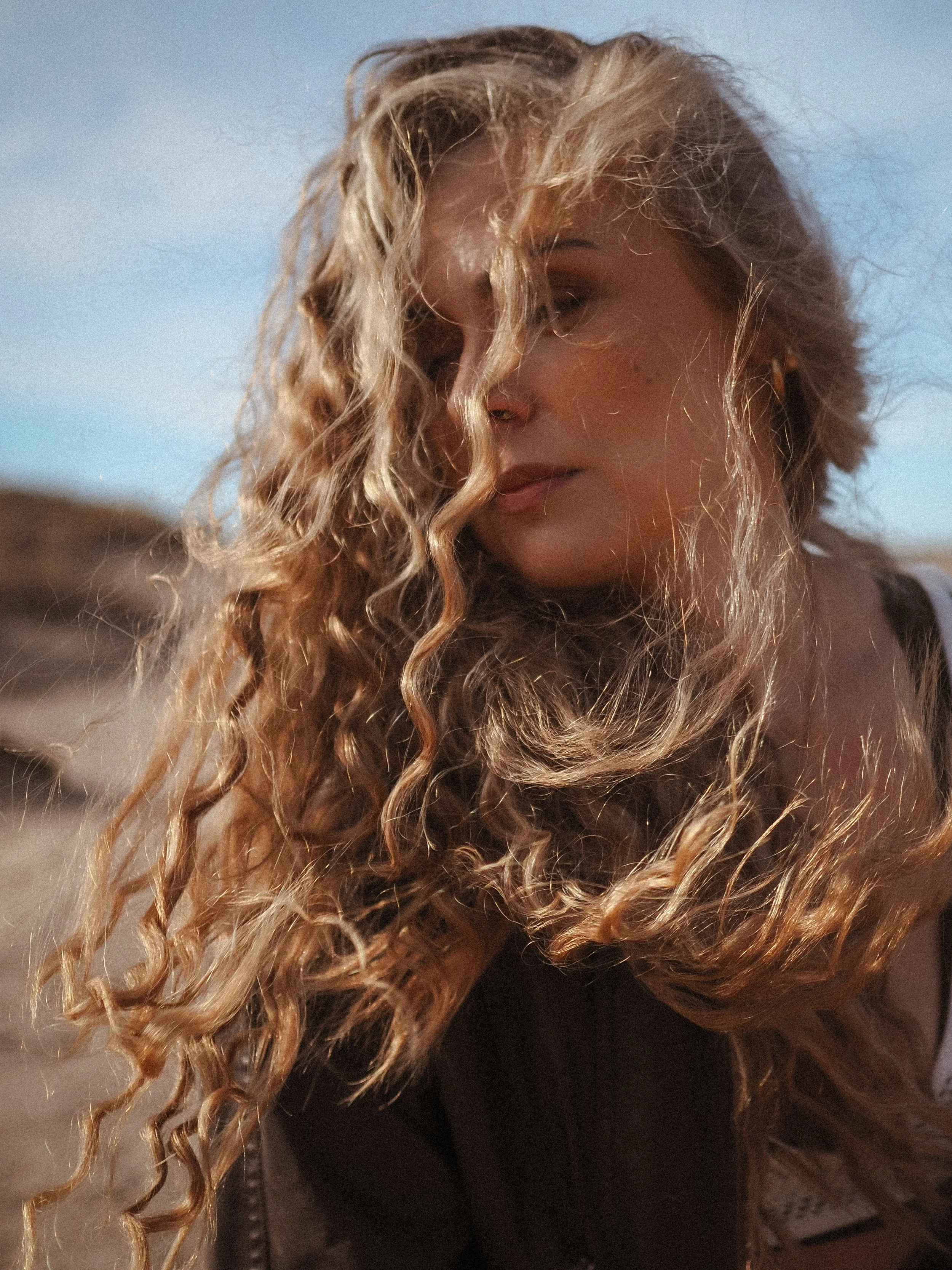 Nainen katsoo alas, taustalla sininen taivas ja maasto.