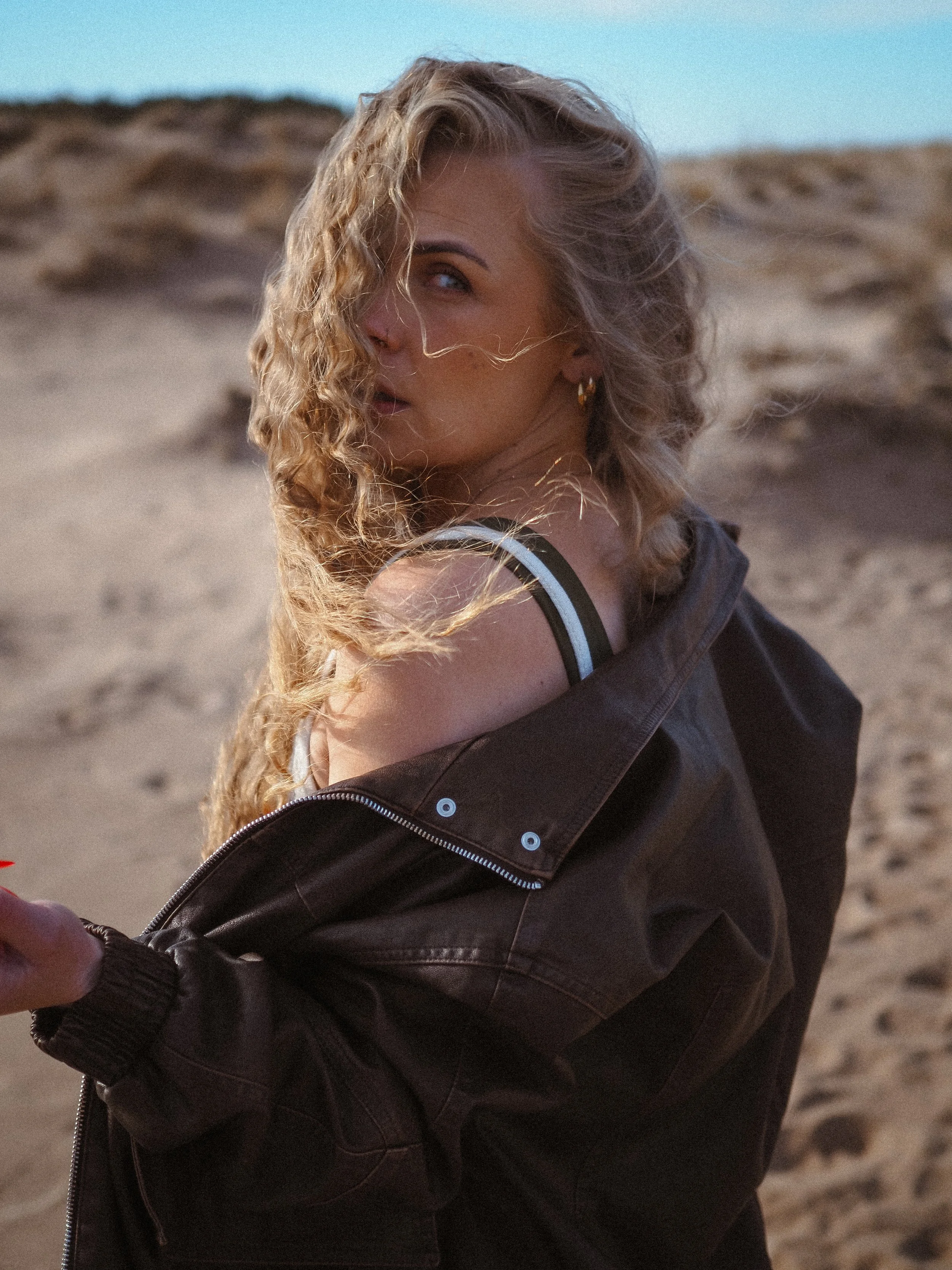 Nuori nainen hymyilee maastossa, takana hiekka ja taivas.