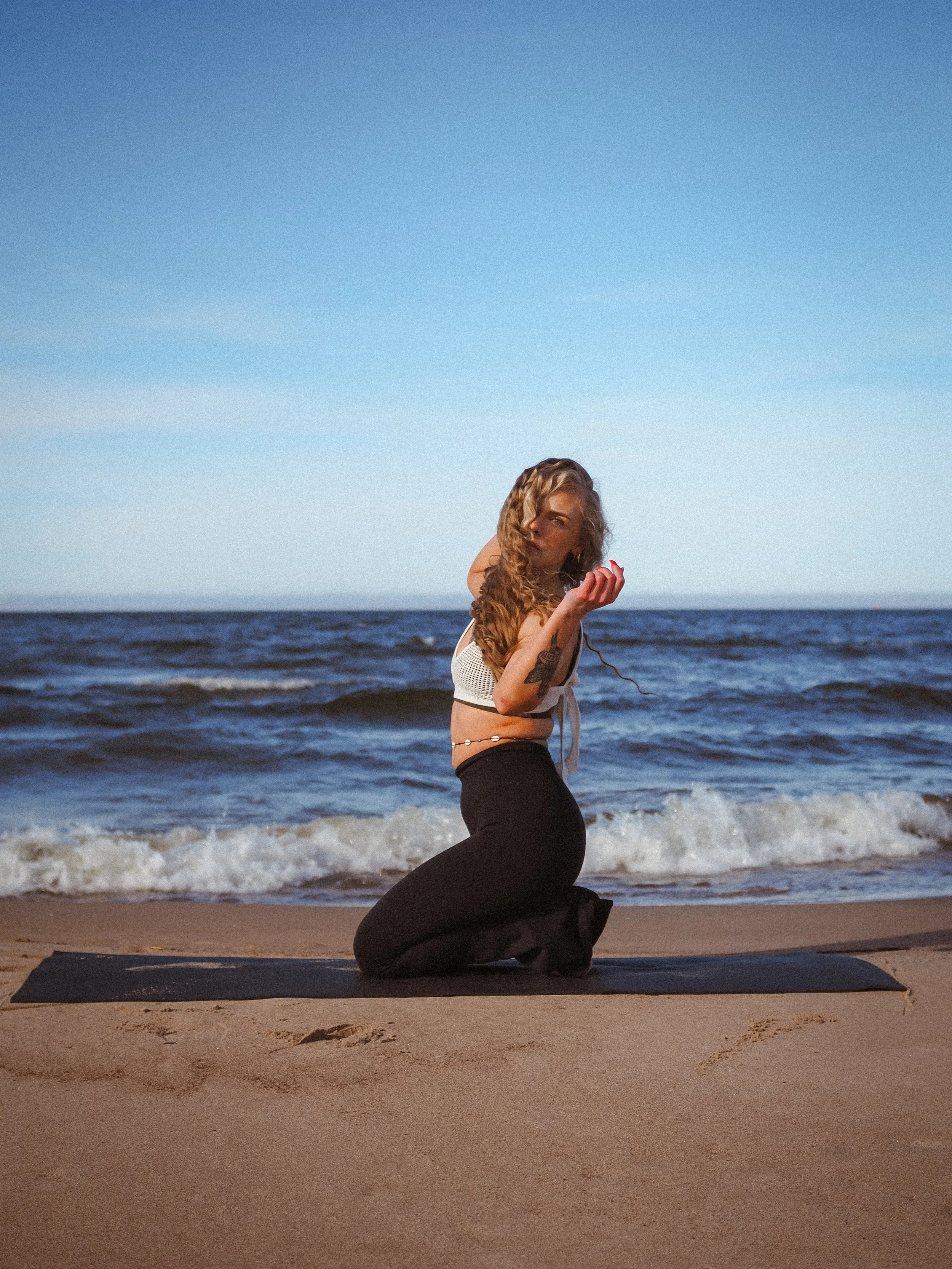 Nainen polvillaan rannalla joogamatolla, meren ja taivaan taustalla.
