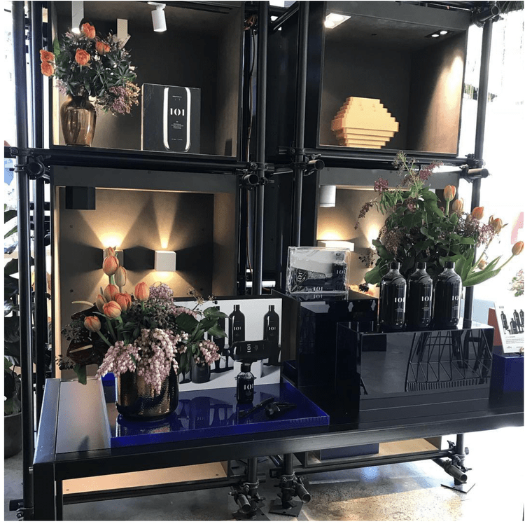 Display shelf with flowers, perfume bottles, and a product box, set up for a promotional event.