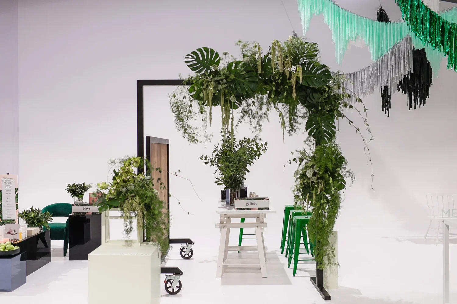 Interior scene with green plants, white furniture, and colorful decorations, possibly at an event or showroom.