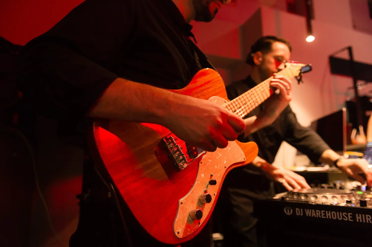 Musicians playing guitar and keyboard in a dimly lit performance space with red lighting.