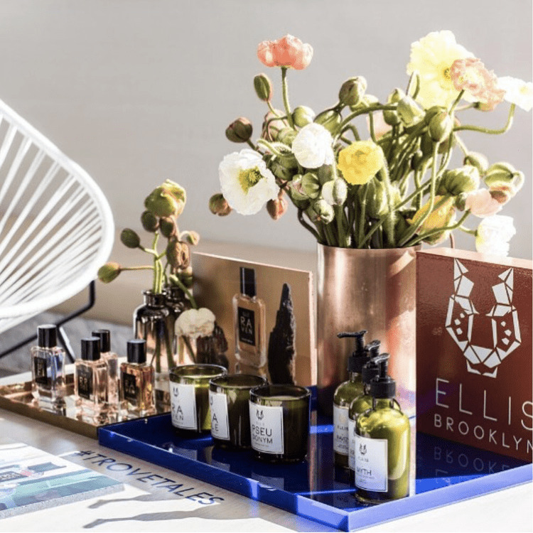 A display of skincare products, candles, and a flower arrangement in a copper vase on a table.