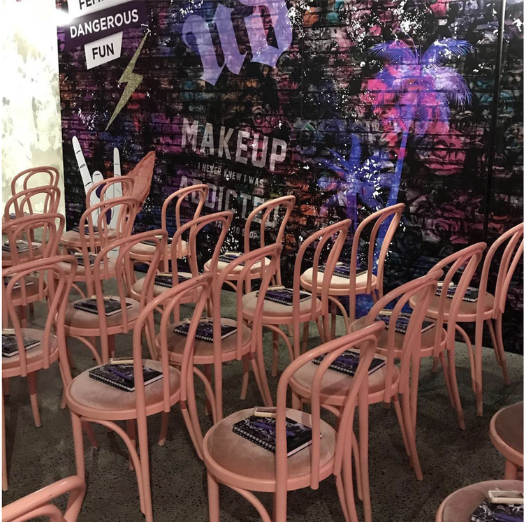 Multiple pink chairs arranged in rows facing a colorful, graffiti-style wall with various words and graphics.