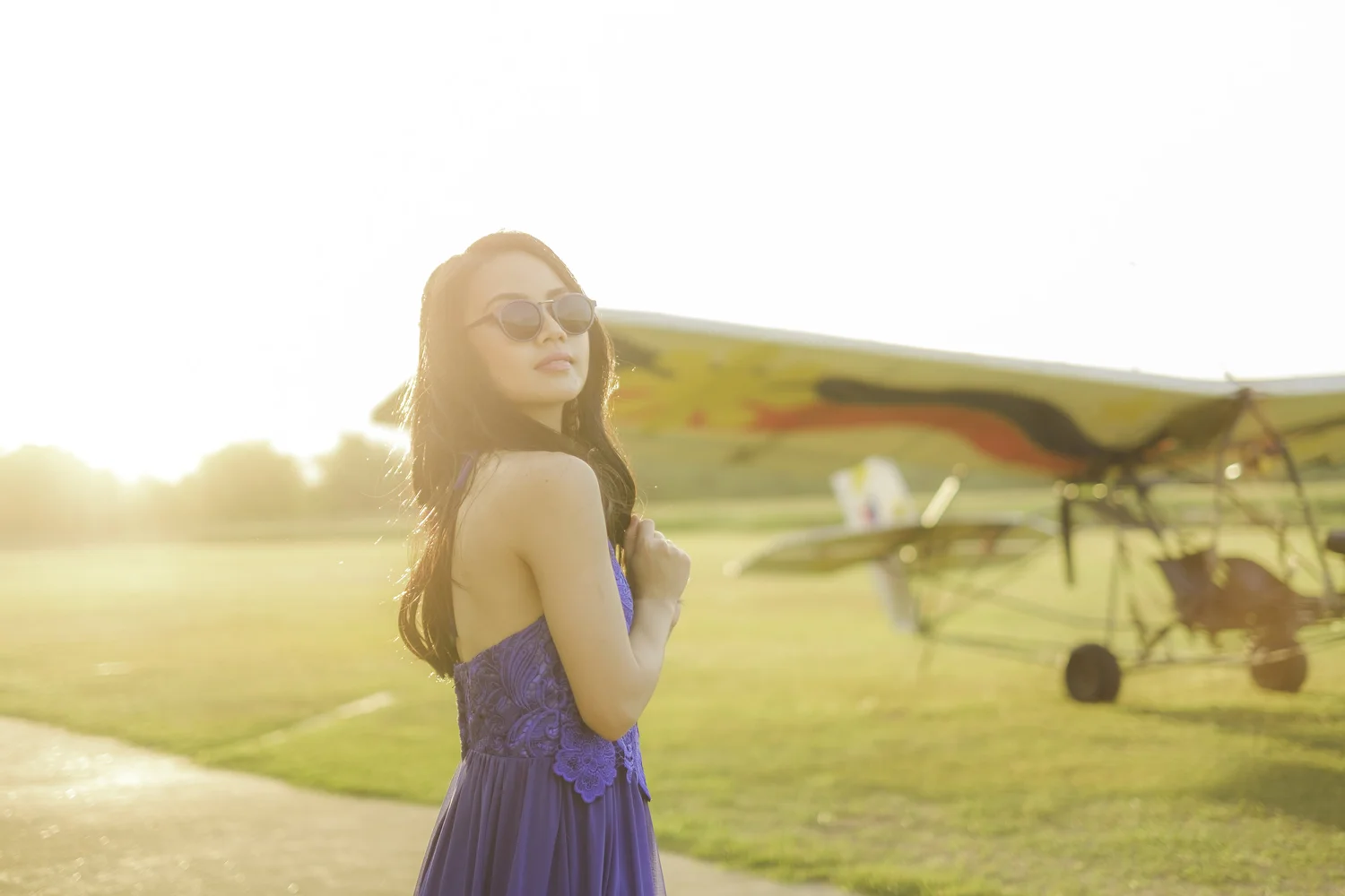 Sunlit outdoor portrait of a woman in a blue dress beside an aircraft.