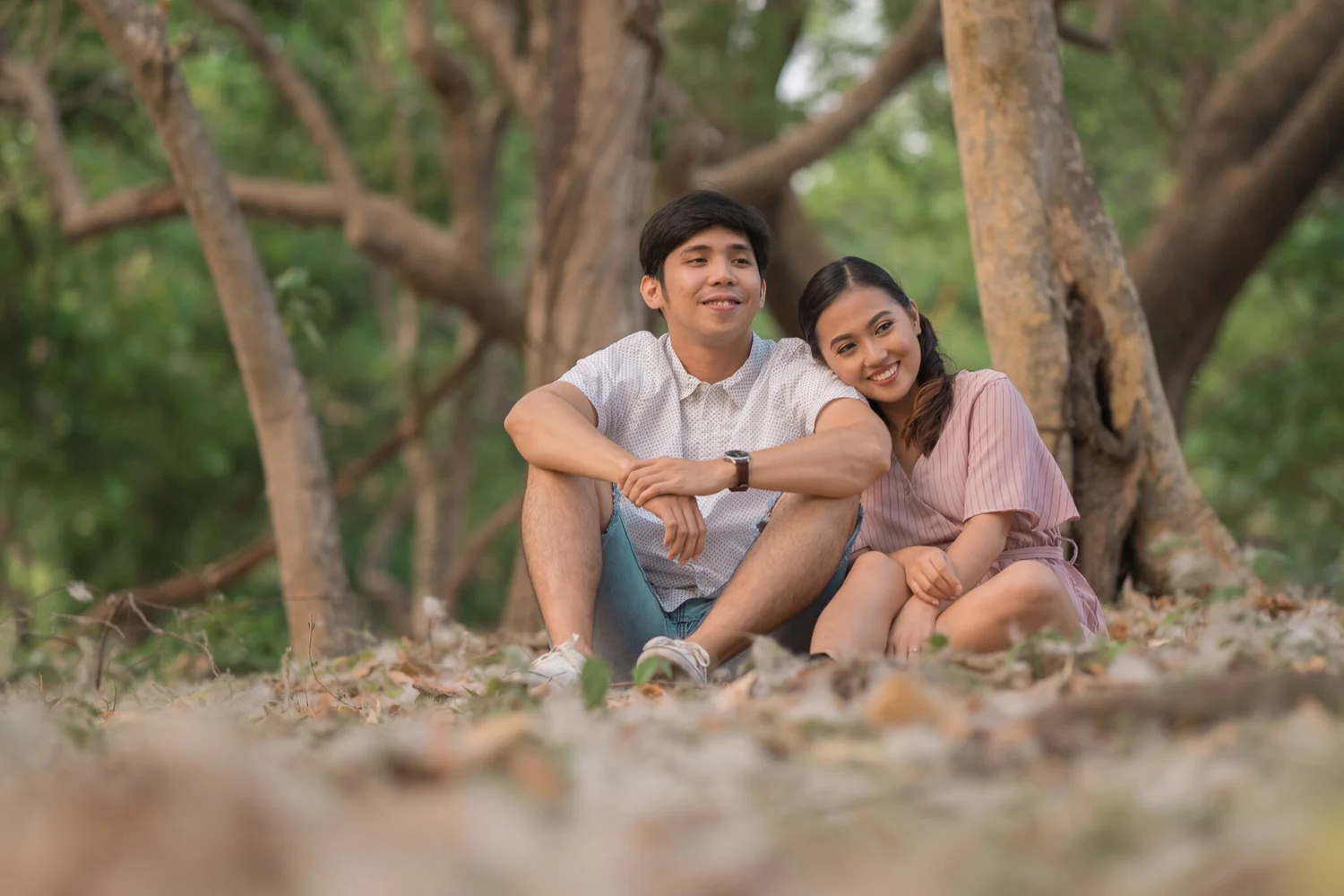 Couple seated together outdoors beneath a tree.