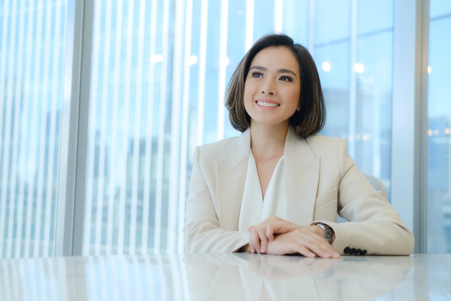 Professional portrait of a woman in a light suit beside an office window.