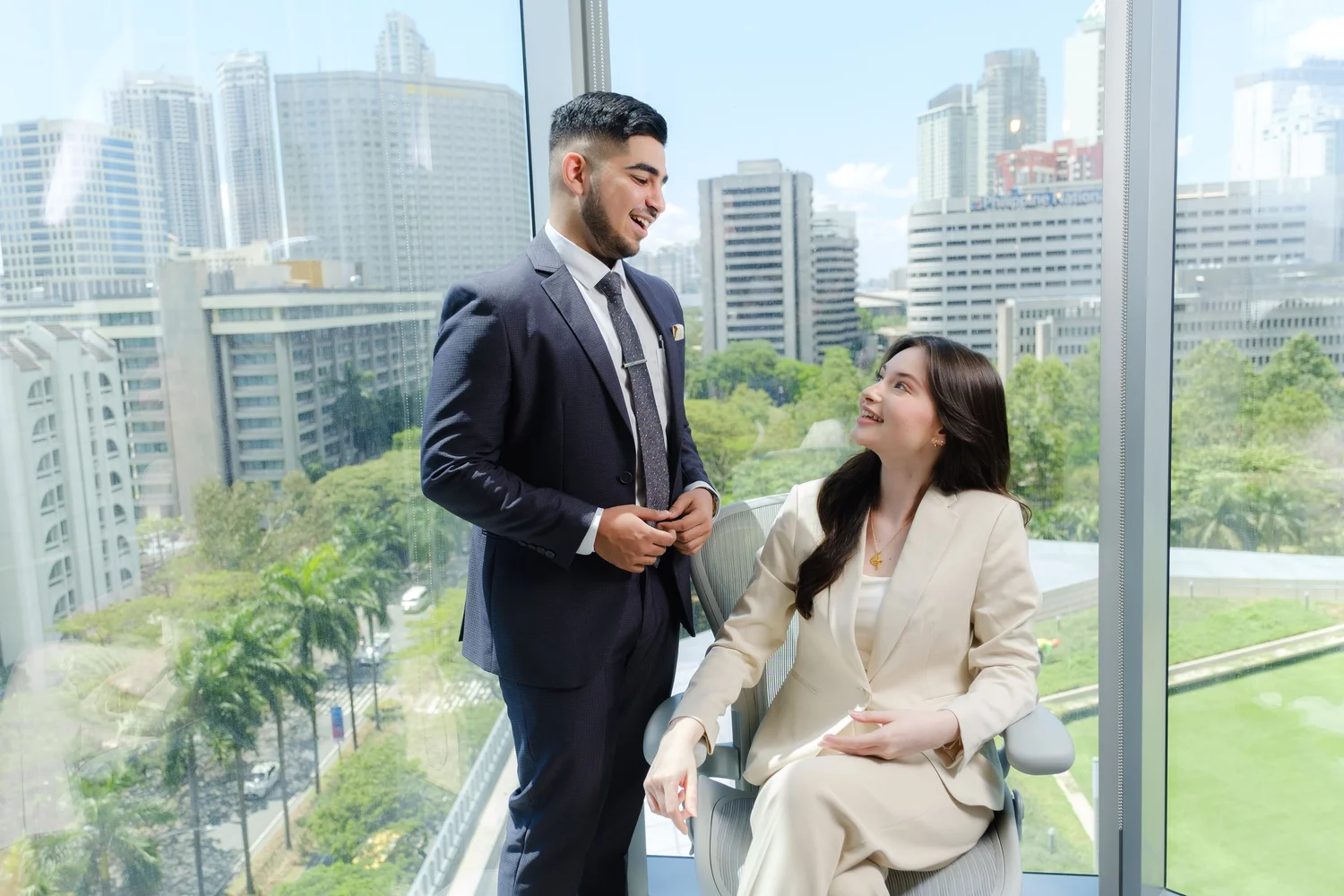 Two professionals in an office with city views.