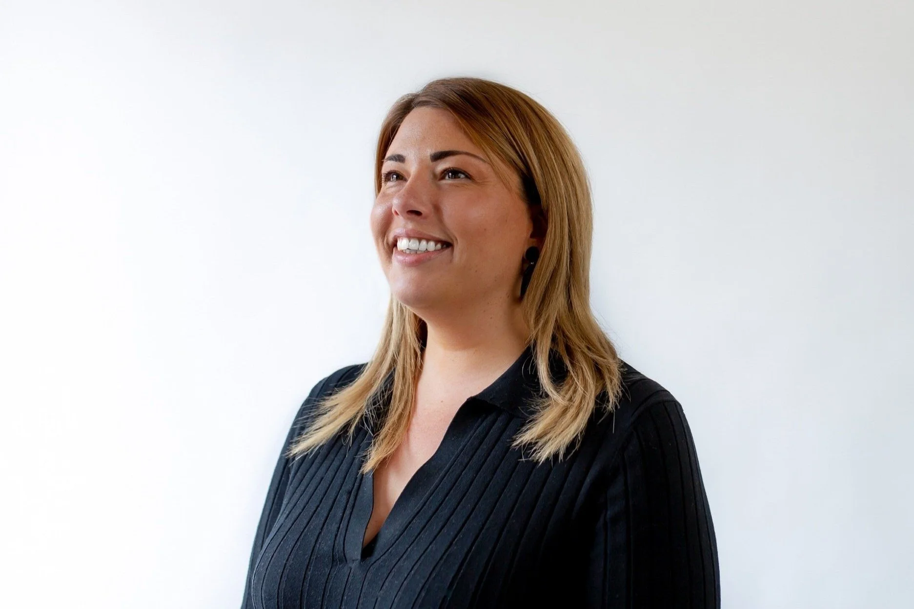 A photo of Heather Arnell, Company Director at Williams Gallagher, smiling and looking slightly to the left, wearing a black pinstripe blouse, standing against a plain light-coloured background.