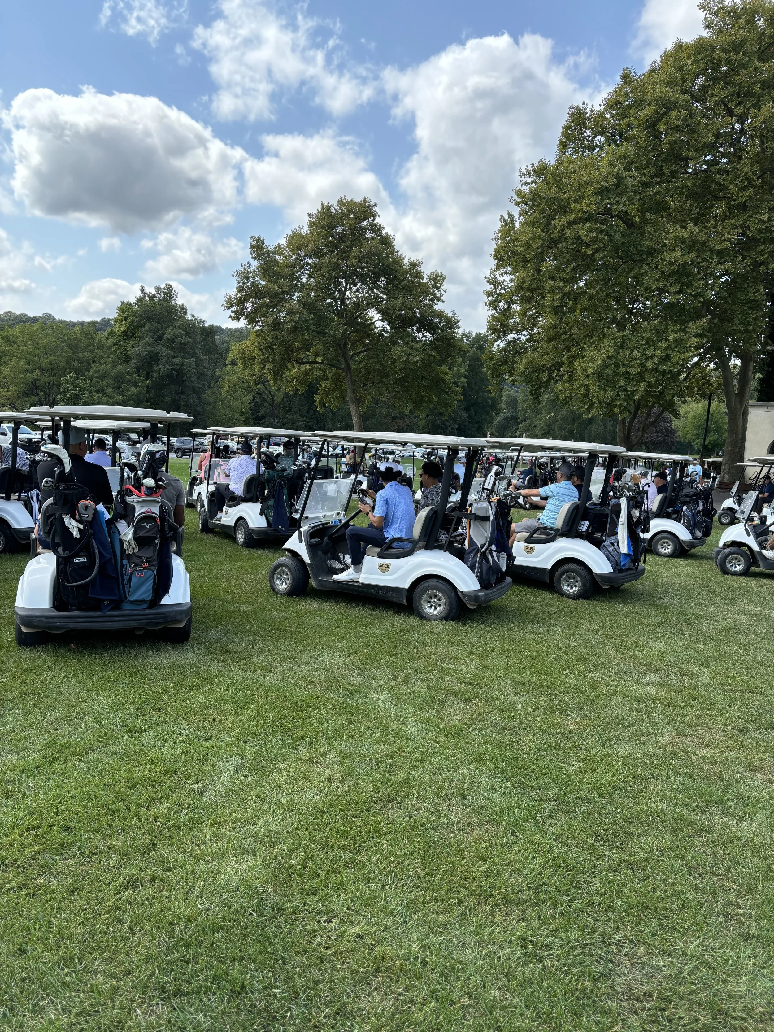 Golf carts with people on a grassy field near trees.
