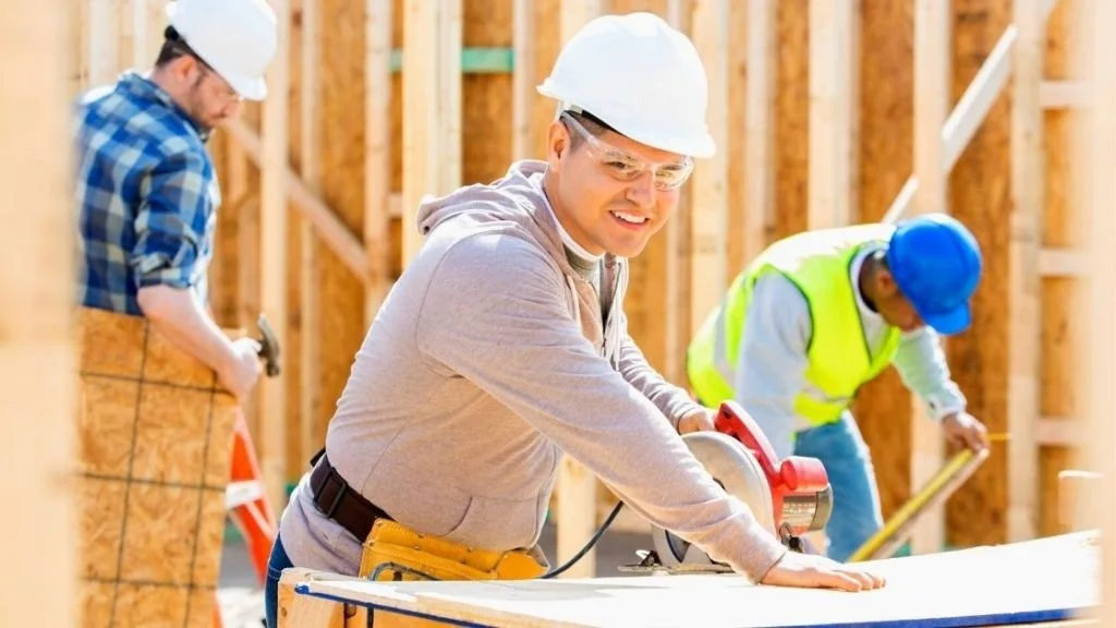 Construction workers in hard hats using tools at a building site.