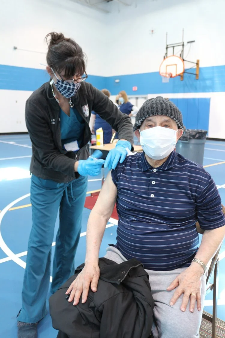 Healthcare worker administering a vaccine to an elderly person in a gymnasium.