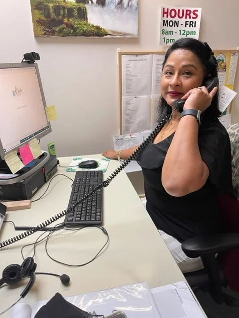 Woman at a desk talking on a phone, with computer and office supplies around her.