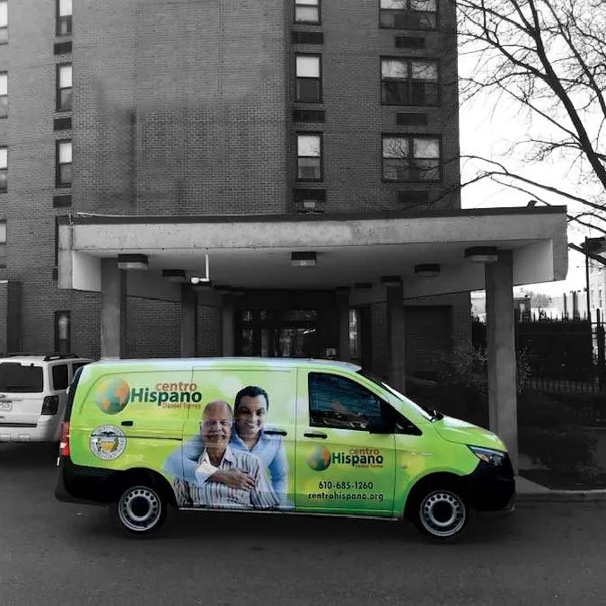 Centro Hispano van parked in front of a building, featuring vibrant branding and logo on its side.