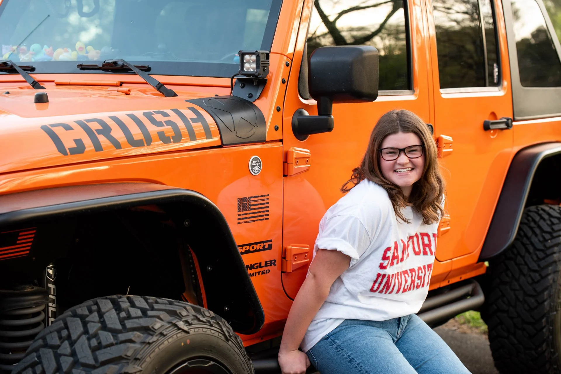 High school senior leaning on orange Jeep Wrangler in Samford University shirt, Pell City Alabama senior photos by Darling Dear Photo