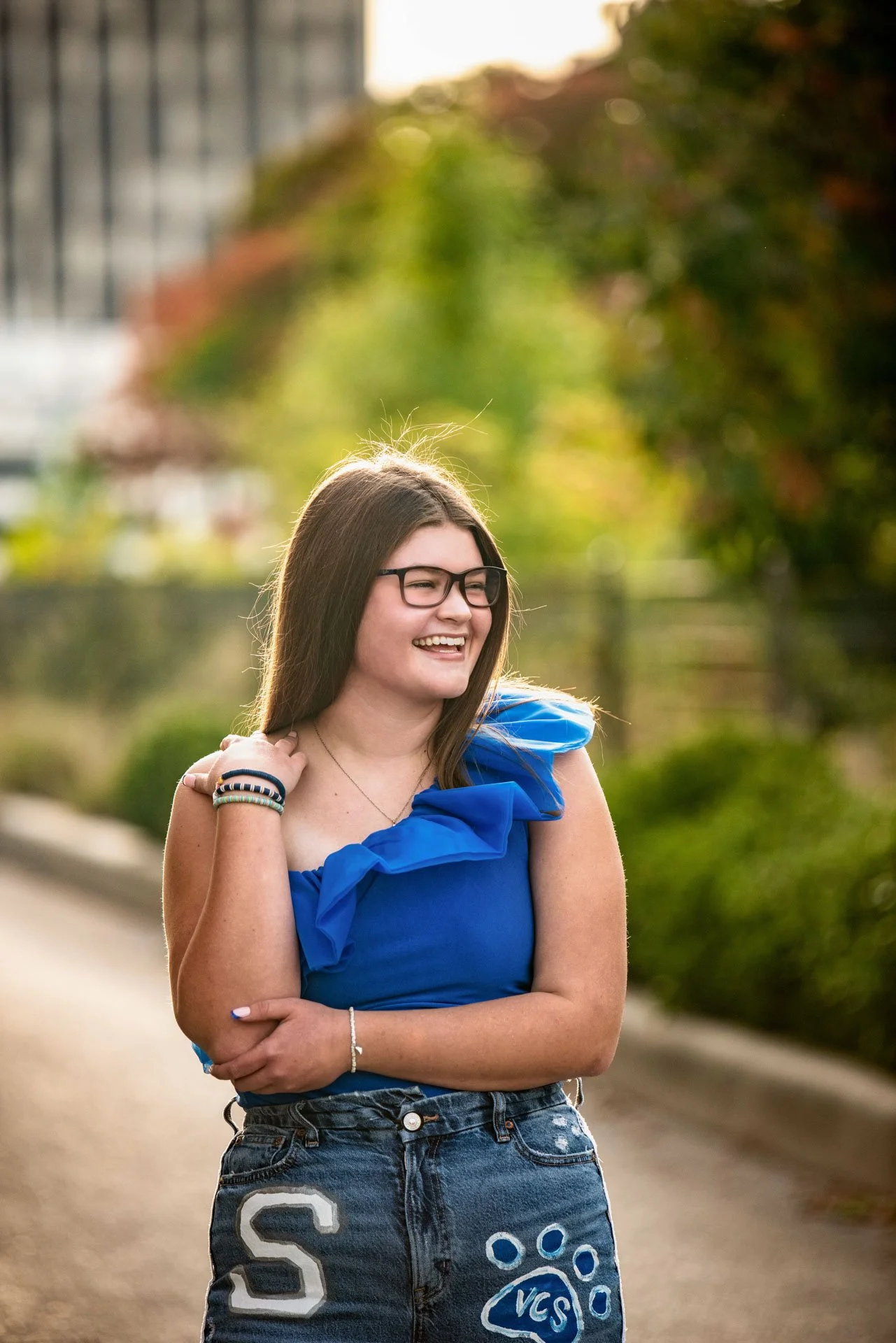 Senior girl in blue top walking Birmingham tree-lined street with custom senior jeans, Darling Dear Photo