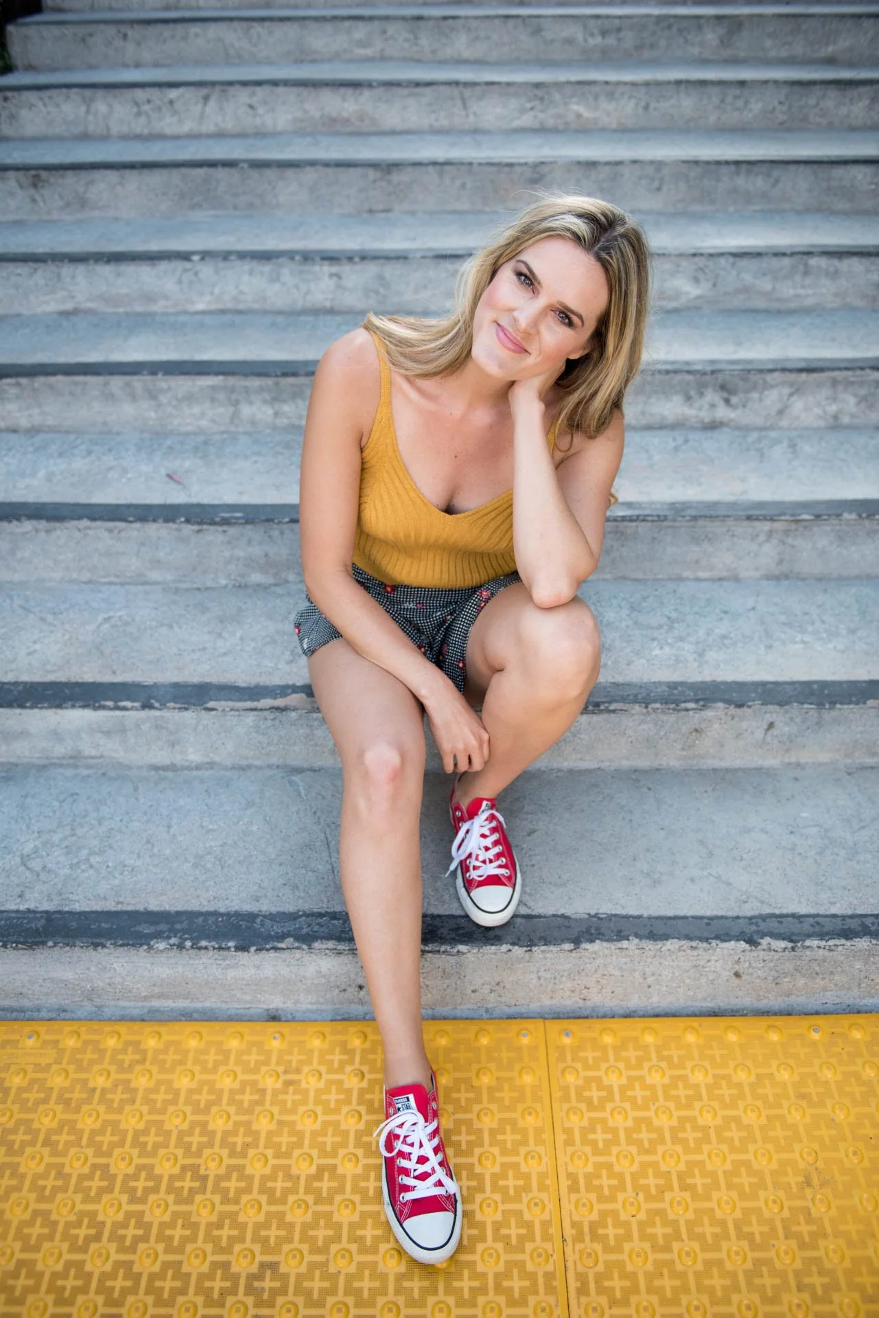 Kristin sitting on steps in a yellow top with red shoes and a yellow crossing line under her feet for her personal branding session